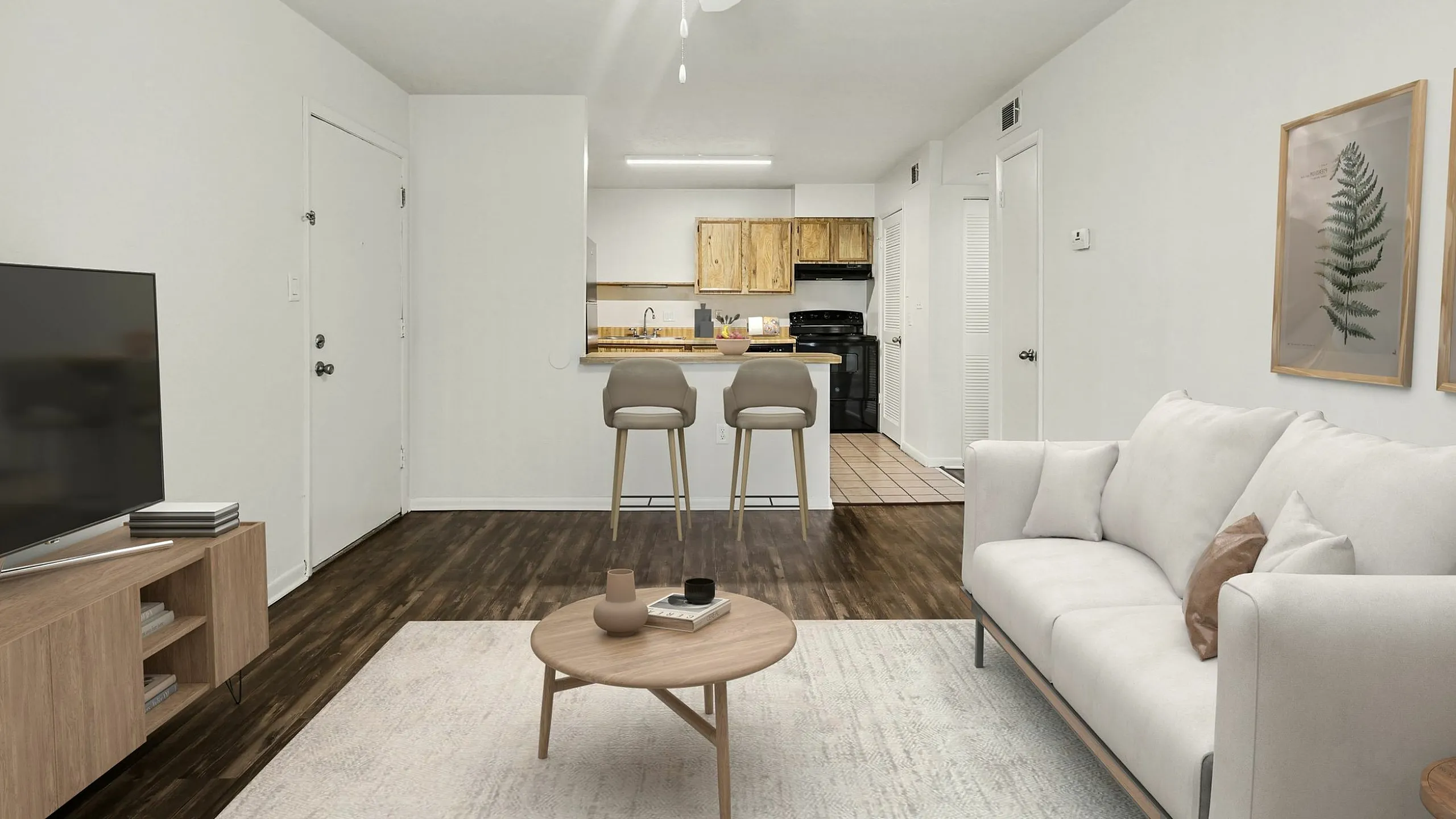Modern living room with sleek wood flooring, cozy white sofa, and minimalist decor, leading to an open kitchen with bar seating.