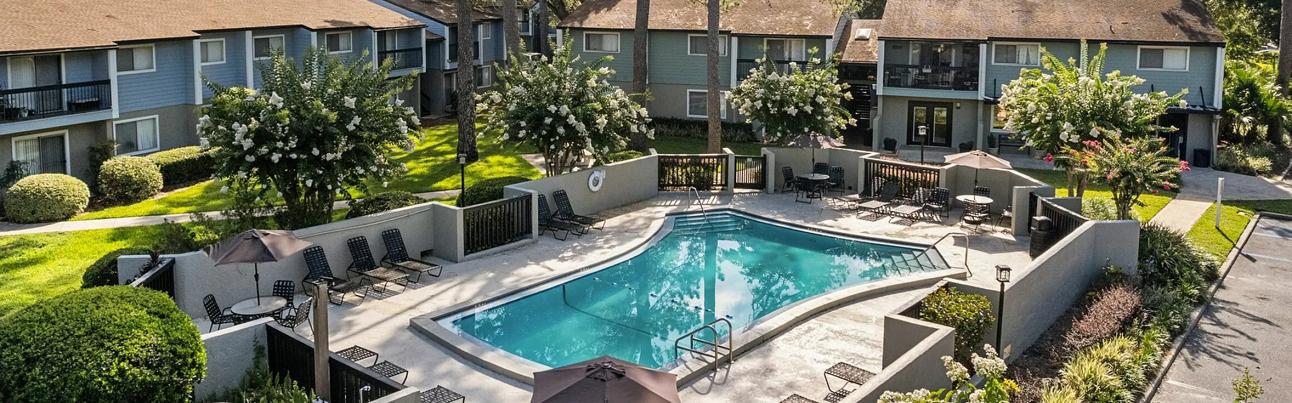 Charming apartment complex featuring a refreshing pool surrounded by lush greenery and inviting outdoor seating areas.