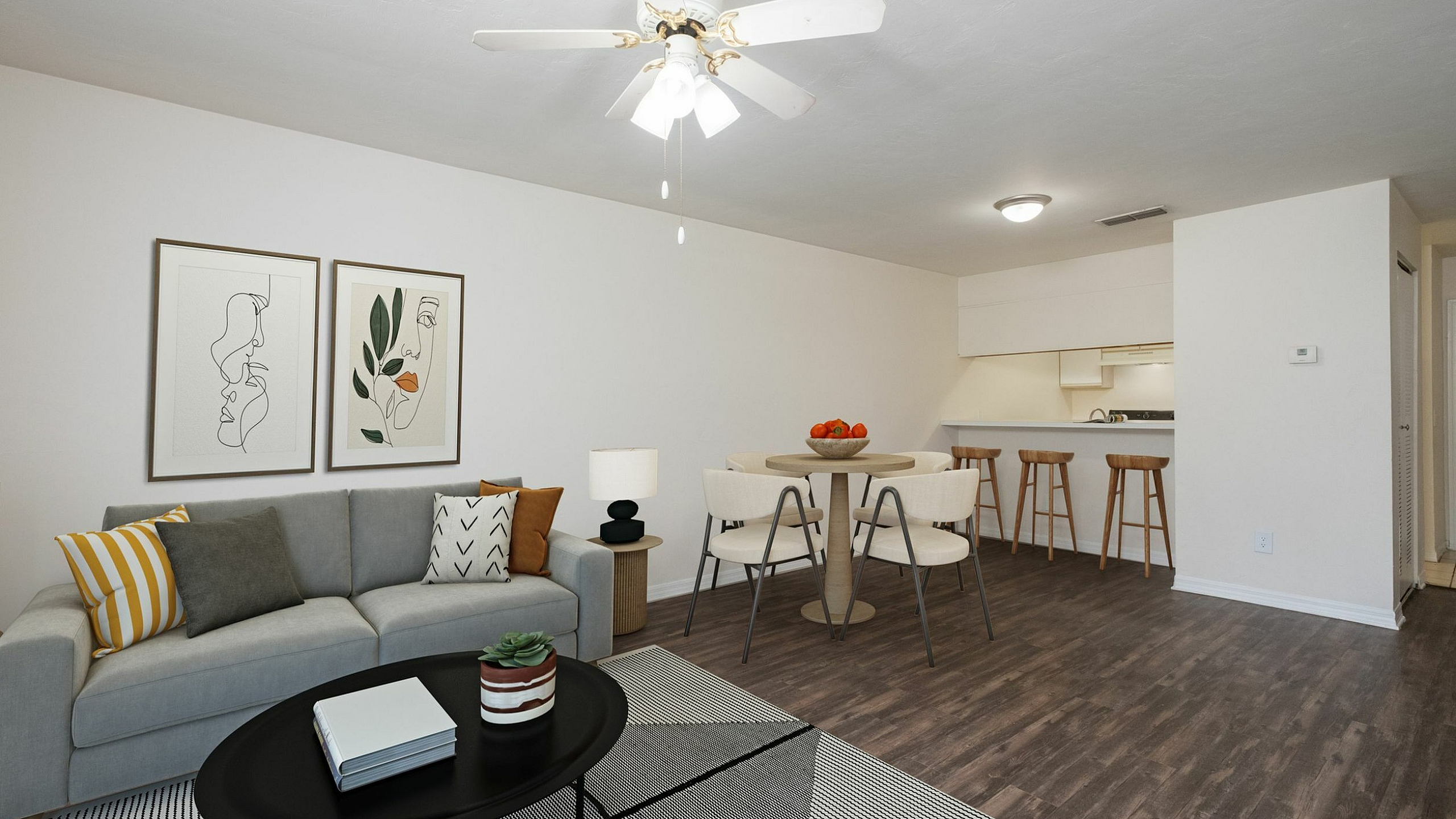 Contemporary open-plan living area featuring a stylish grey sofa with accent pillows, modern artwork, a dining table with chic chairs, and a sleek kitchen bar with stools.