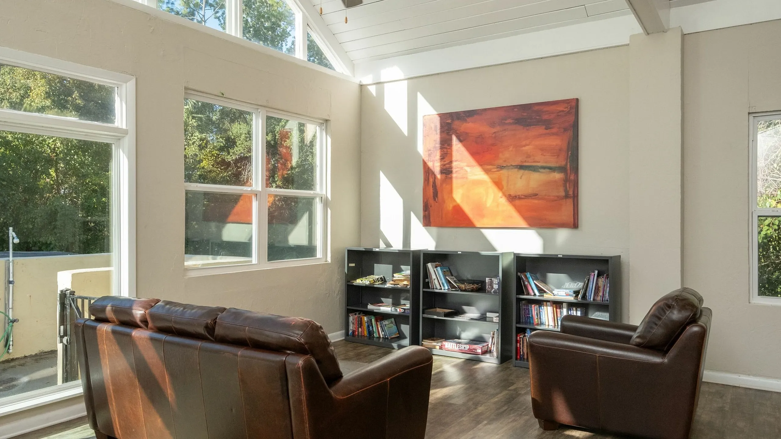 Bright and inviting living room with large windows, showcasing elegant leather furniture and a cozy reading nook with bookshelves.