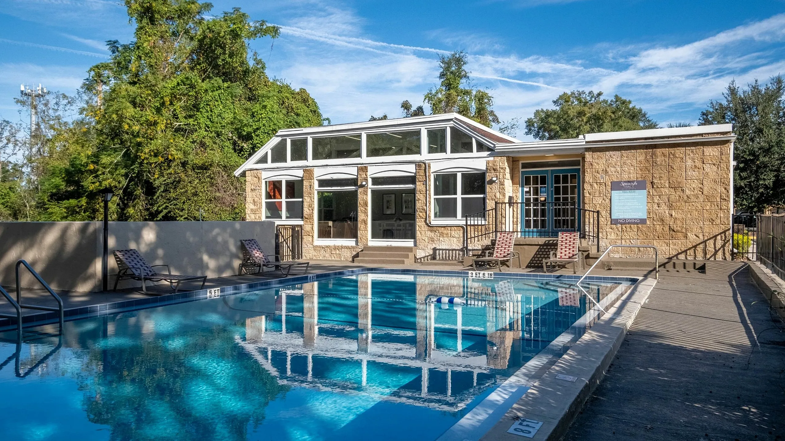 Luxurious outdoor pool area with elegant lounge chairs, adjacent to a stylish clubhouse under a clear blue sky.
