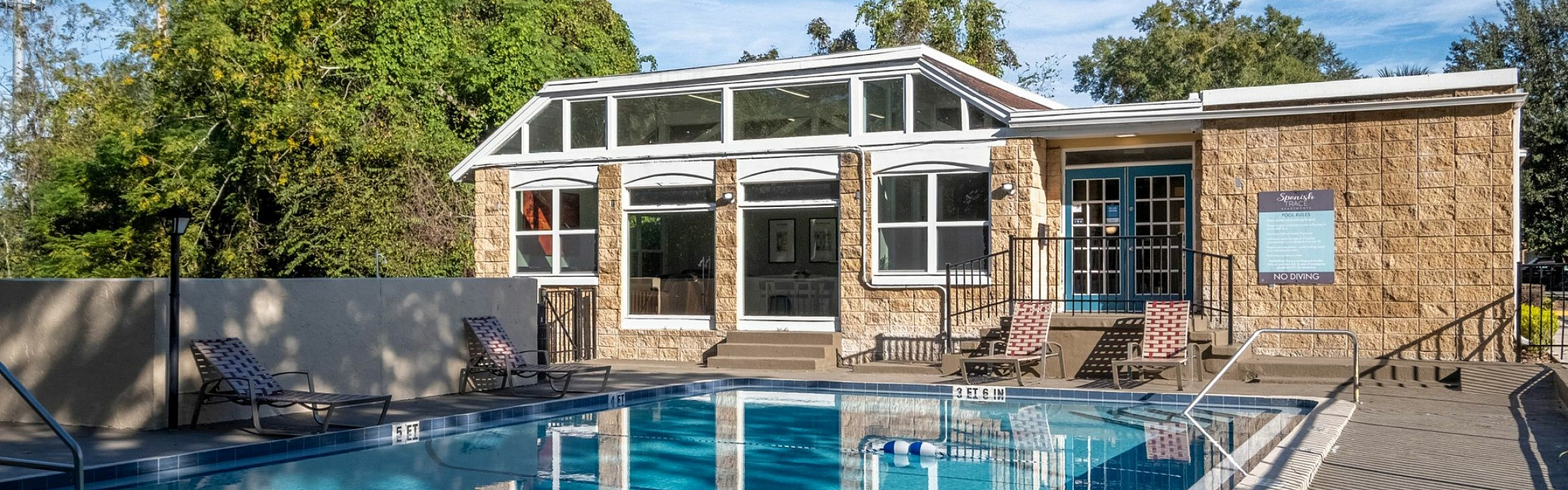 Charming apartment complex featuring a sparkling outdoor pool with lounge chairs and a modern clubhouse surrounded by lush greenery.