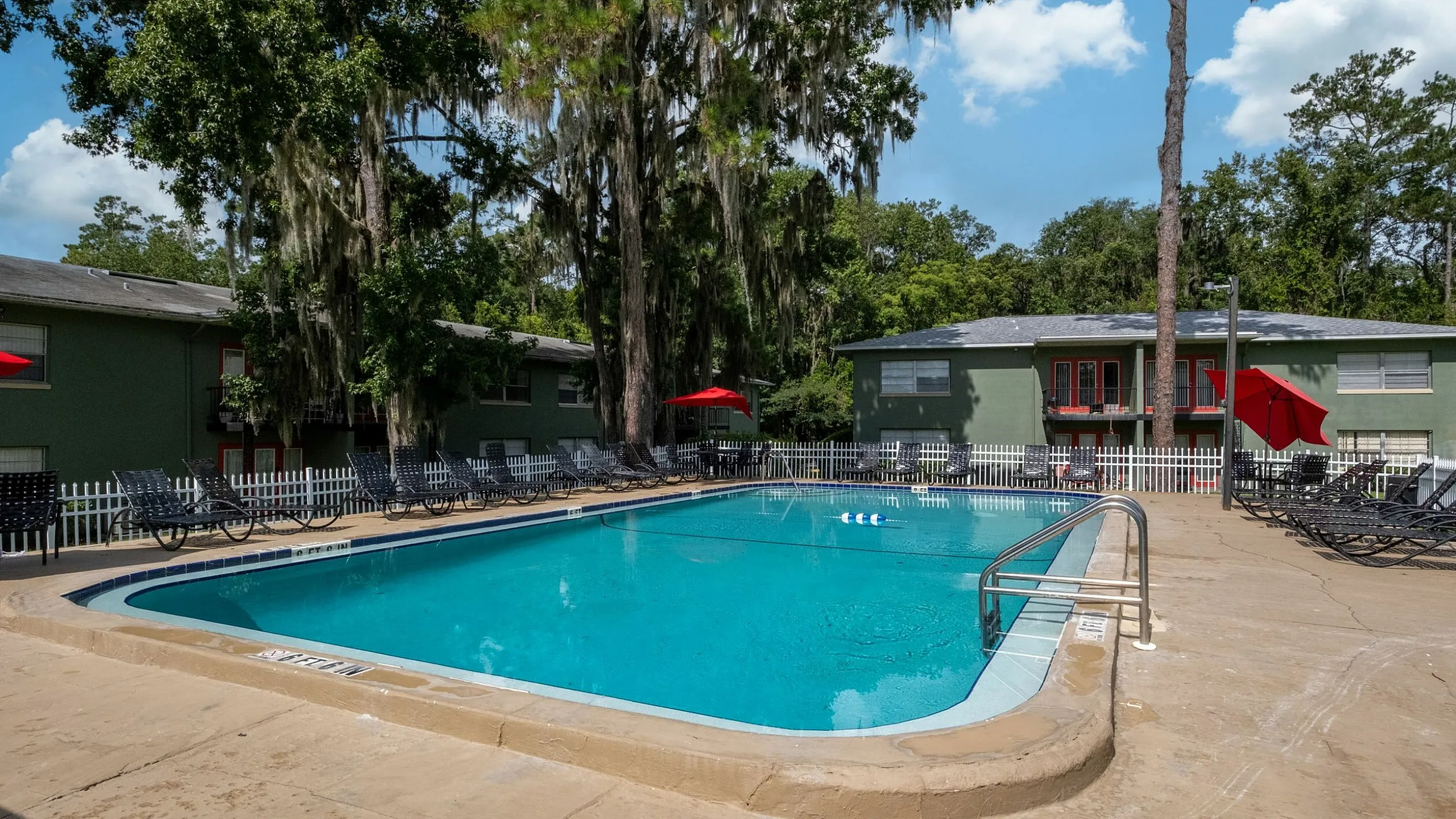 Inviting outdoor swimming pool with surrounding lounge chairs, vibrant red umbrellas, and lush greenery providing a tranquil retreat.