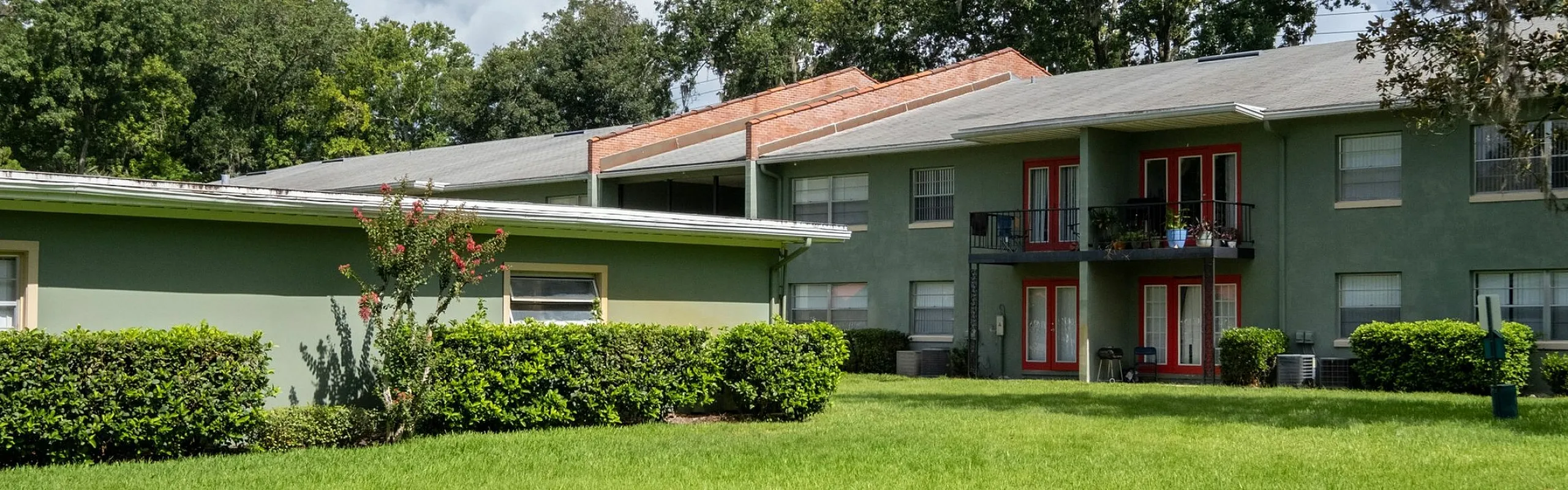 Charming apartment building with lush green lawn, vibrant red accents, and serene surroundings.