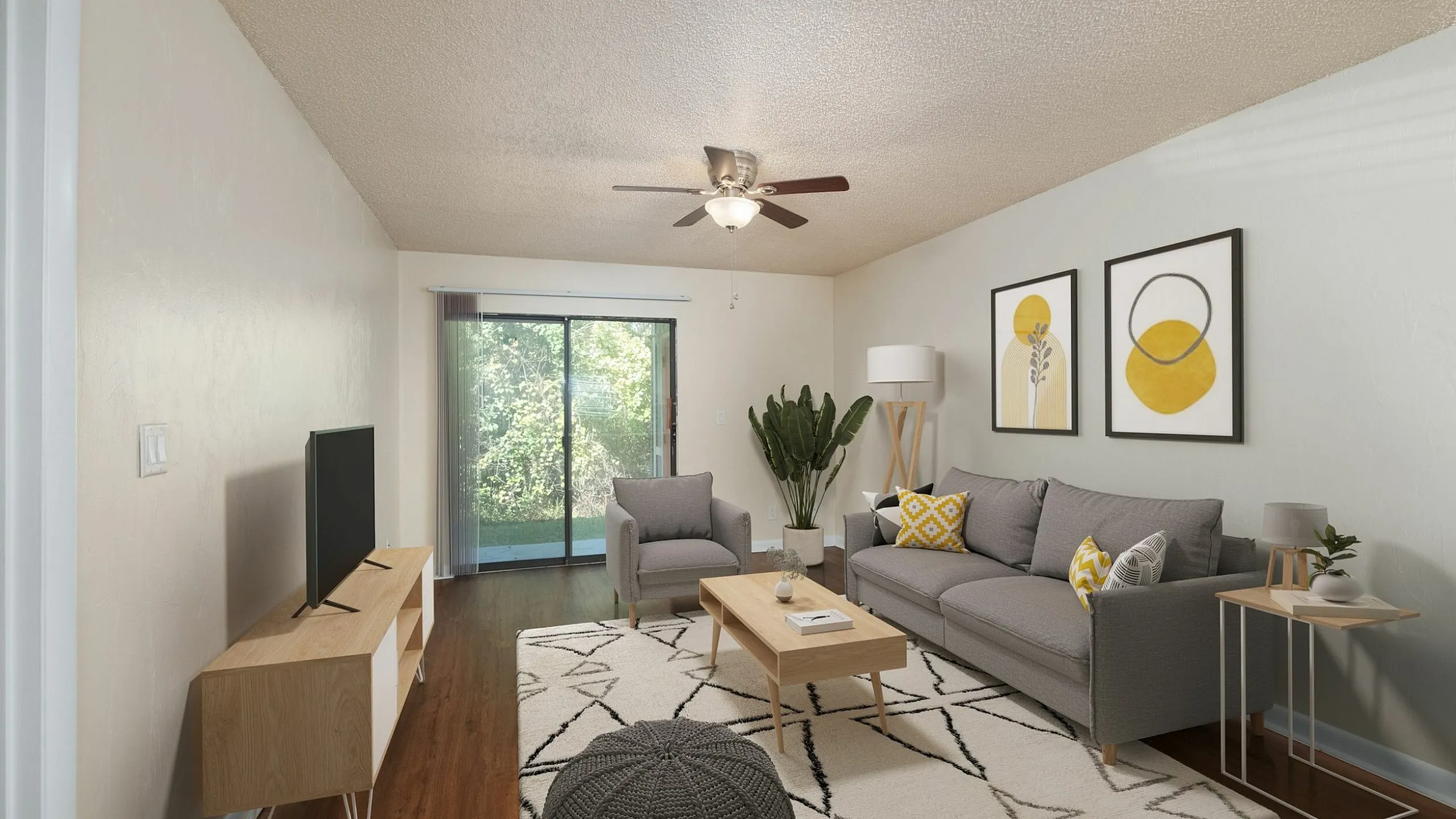 Bright and inviting living room with modern gray furniture, elegant artwork, and a view of lush greenery through glass doors.