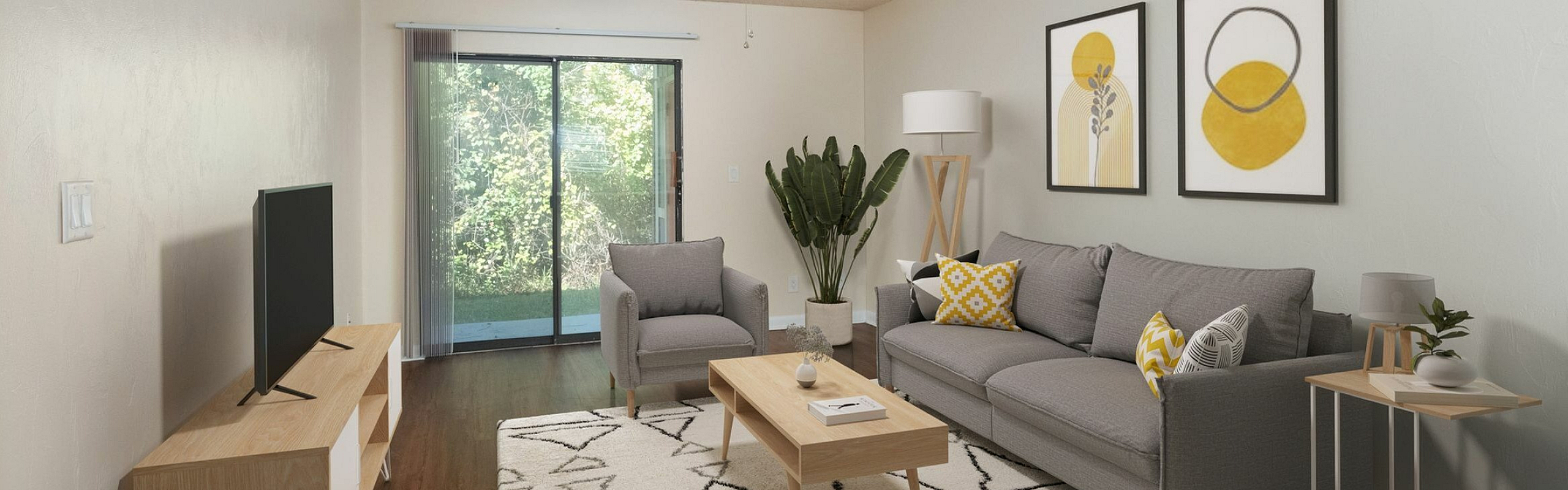 Bright and modern living room featuring elegant gray furniture, stylish decor, and large sliding glass doors leading to a lush outdoor view.