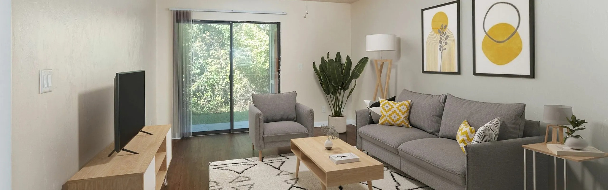 Bright and modern living room with stylish gray furniture, warm wooden floors, and eye-catching yellow accents, leading to a serene outdoor view through glass doors.