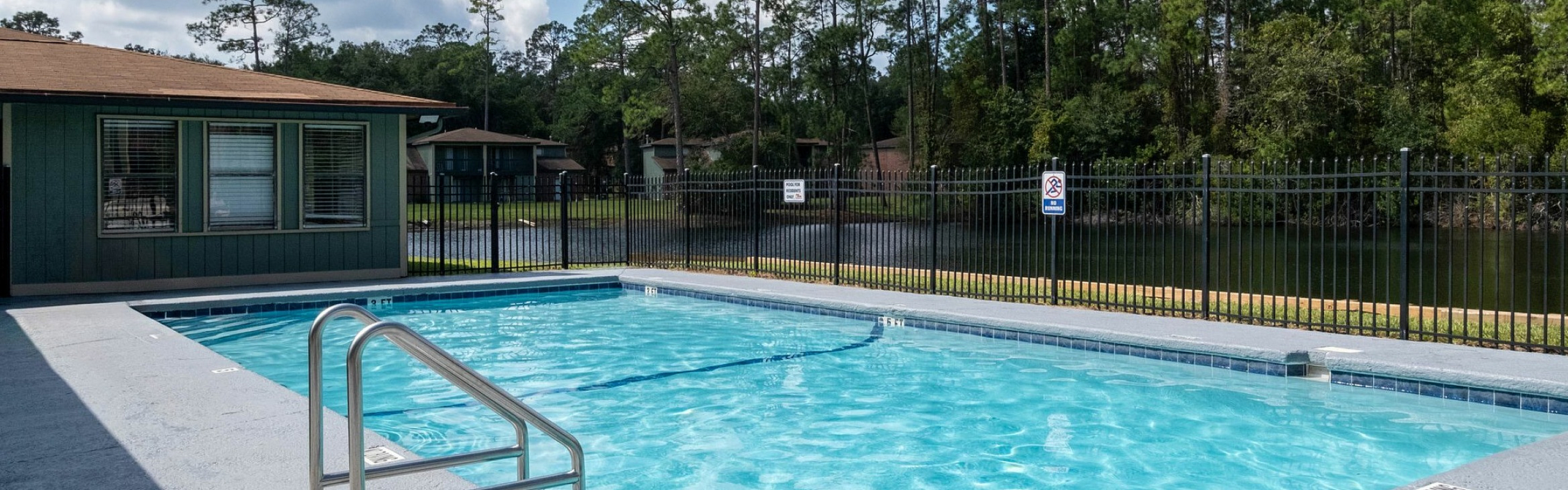 Inviting outdoor pool area with clear blue water, surrounded by lush greenery and bright skies, perfect for relaxation.