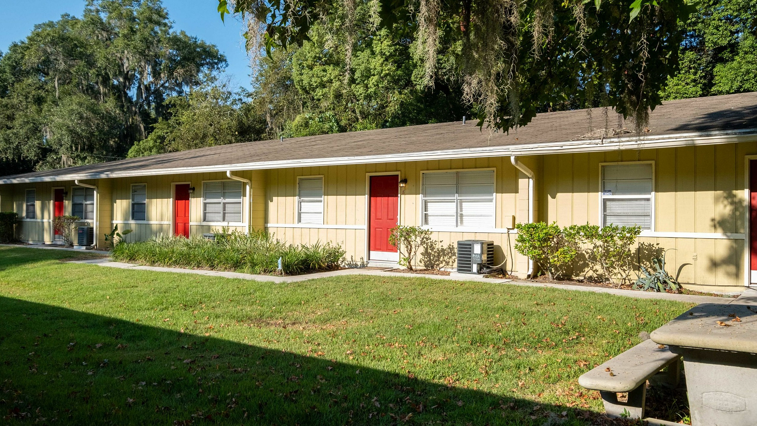 Charming yellow apartment complex with vibrant red doors, set against lush greenery and a sunny, serene backdrop.