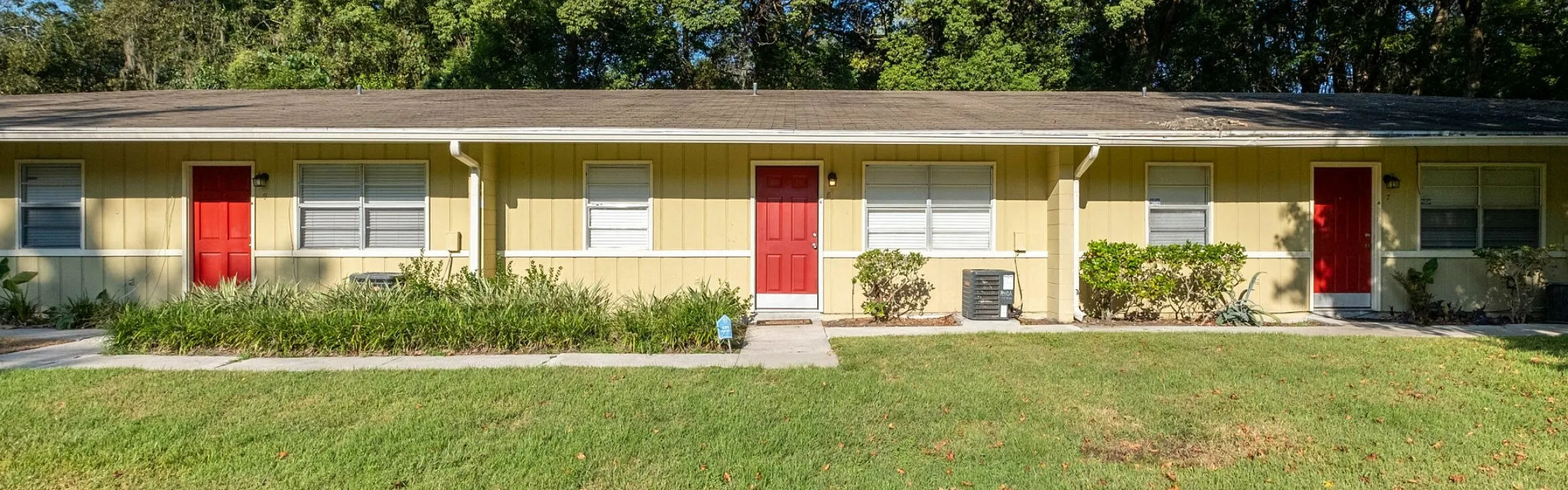 Charming yellow apartment building with bright red doors, nestled in a serene setting with lush green landscaping.