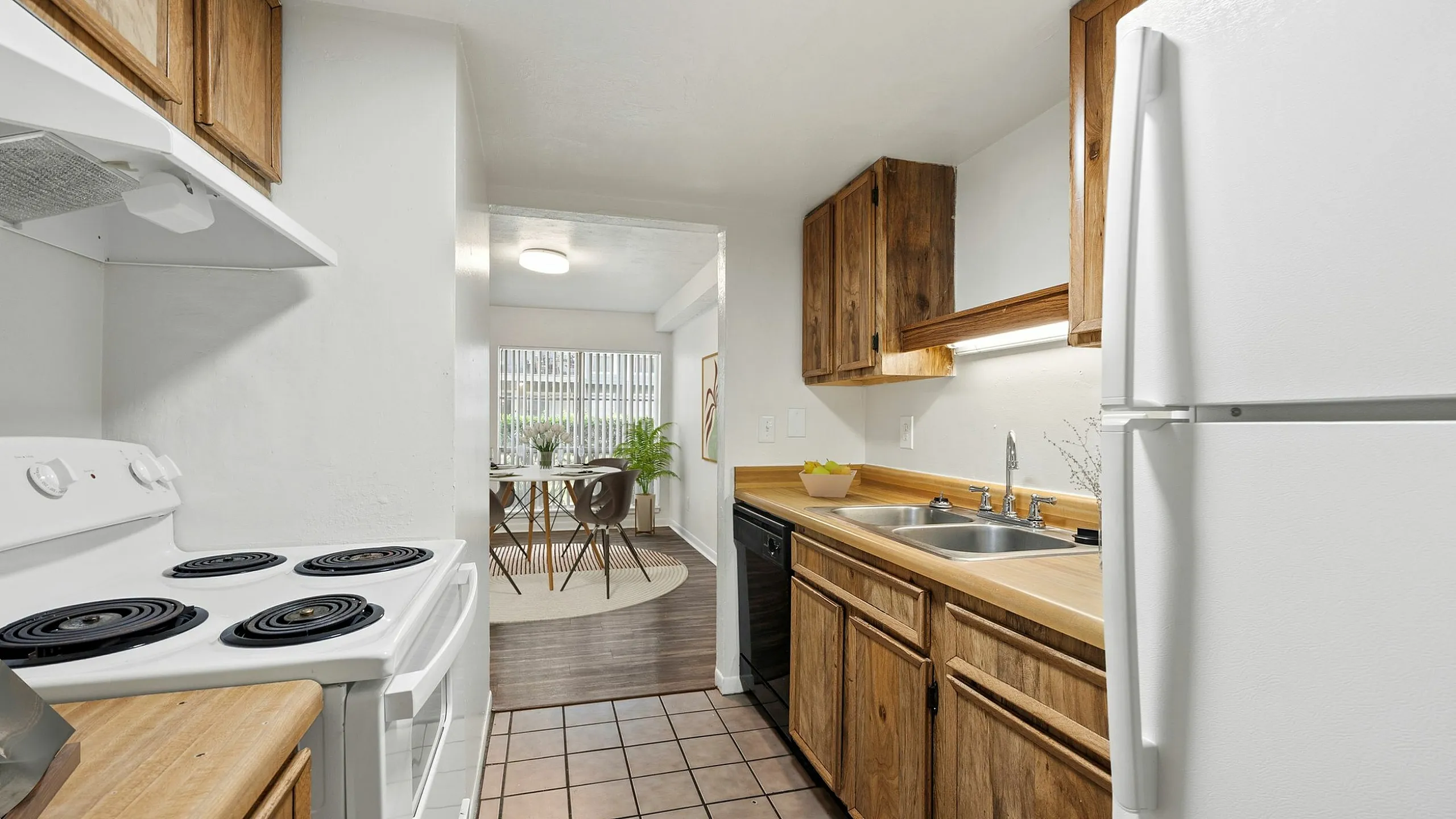 Charming kitchen with warm wooden cabinetry and modern appliances leading to a bright dining area with large windows.