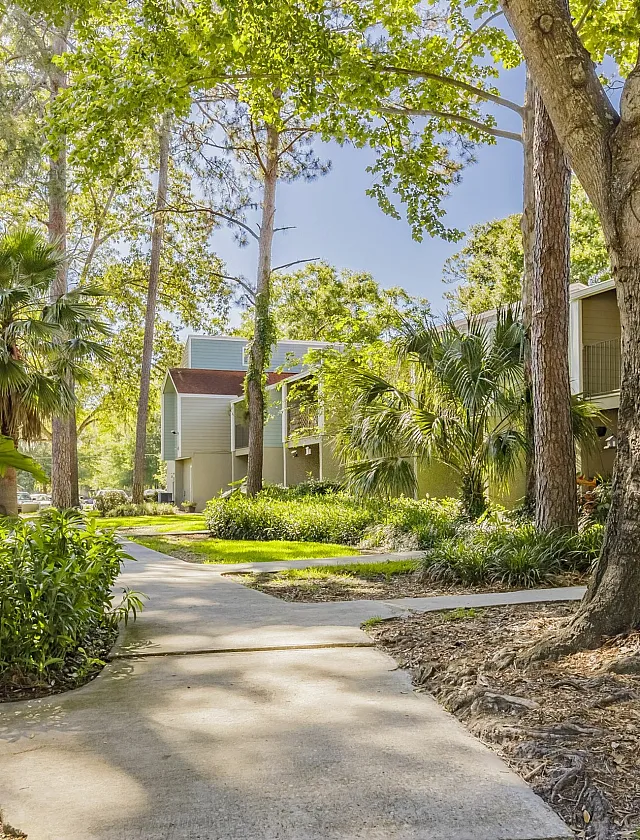Charming apartment complex nestled amongst lush greenery with serene walking paths and majestic trees.