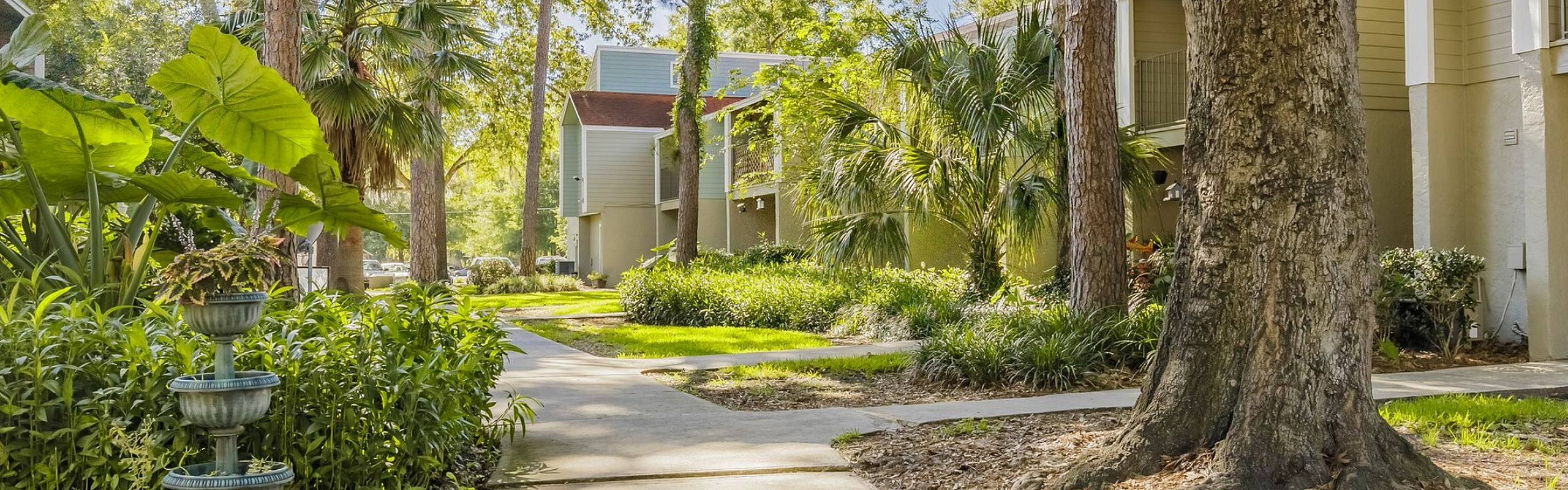 Beautiful apartment complex surrounded by lush greenery and tall trees, offering a serene outdoor environment and inviting walkways.