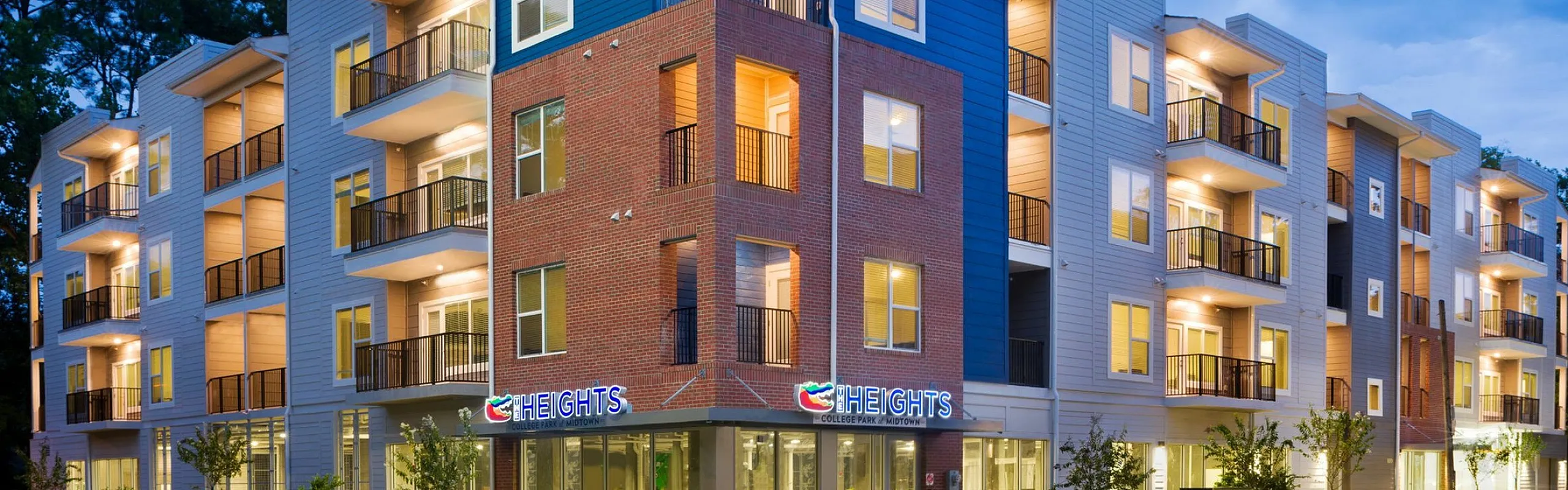 Modern apartment building at dusk with illuminated balconies and stylish architecture, offering vibrant urban living.