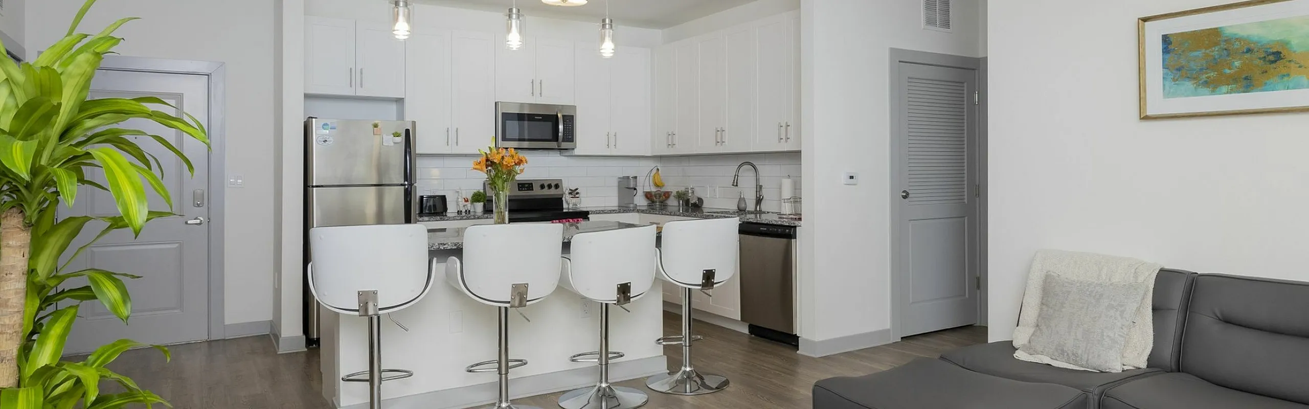 Modern open-concept living space featuring a sleek kitchen with island seating, cozy gray sectional, and vibrant plant decor.