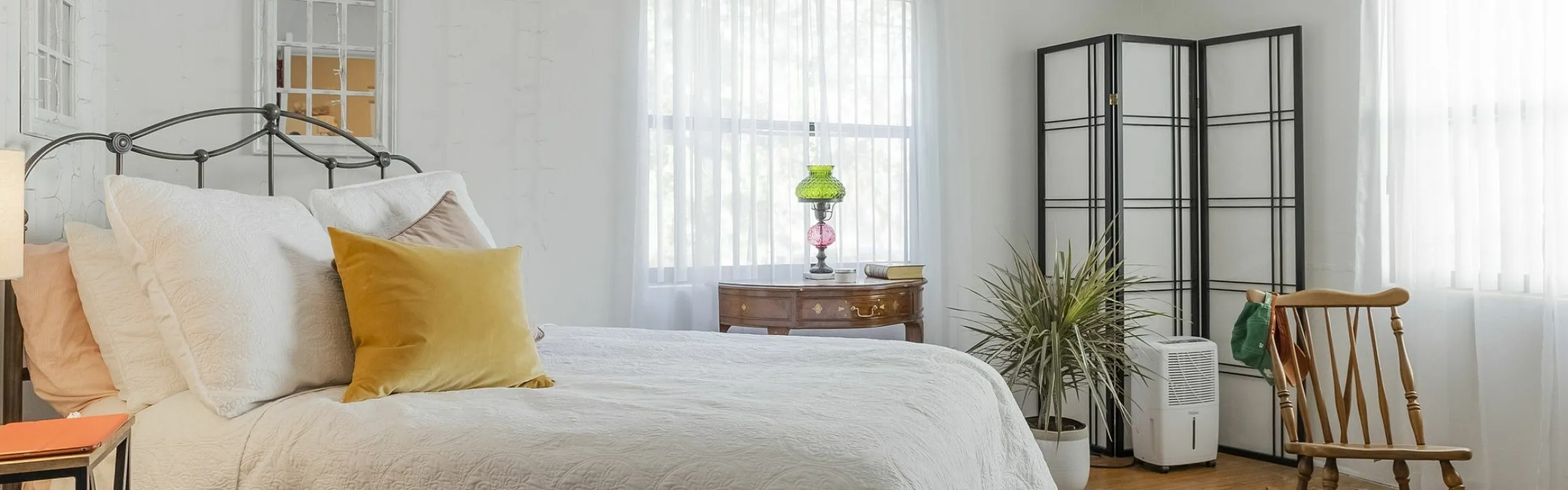 Bright and inviting bedroom with a cozy double bed, elegant ceiling fan, and natural light streaming through large windows, creating a serene atmosphere.