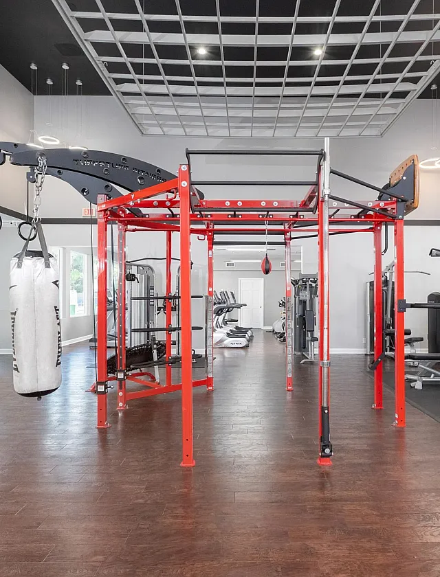 Modern fitness center featuring a red multifunctional exercise frame, punching bag, and various workout machines under stylish lighting.