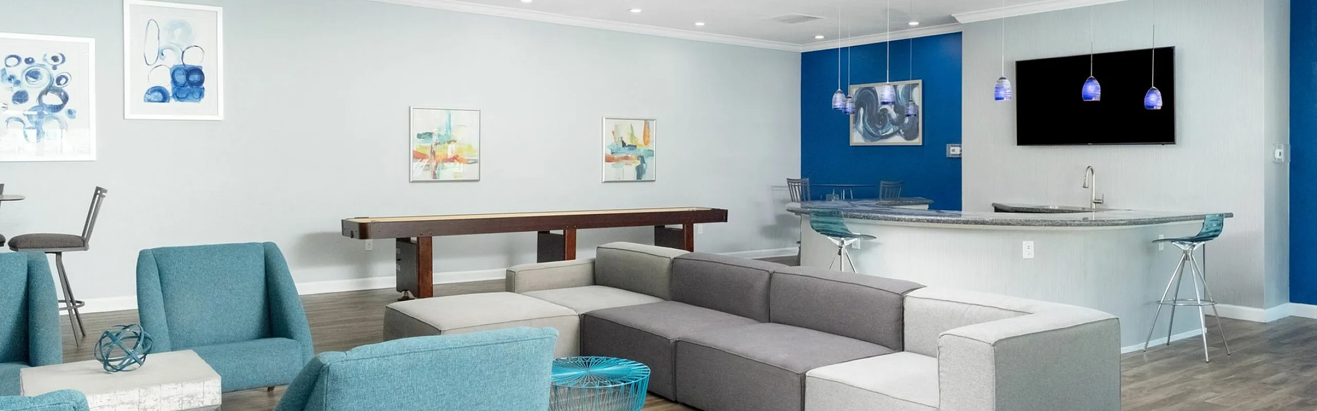 Modern community lounge with stylish blue accents, comfortable seating, a sleek bar area, and contemporary artwork.