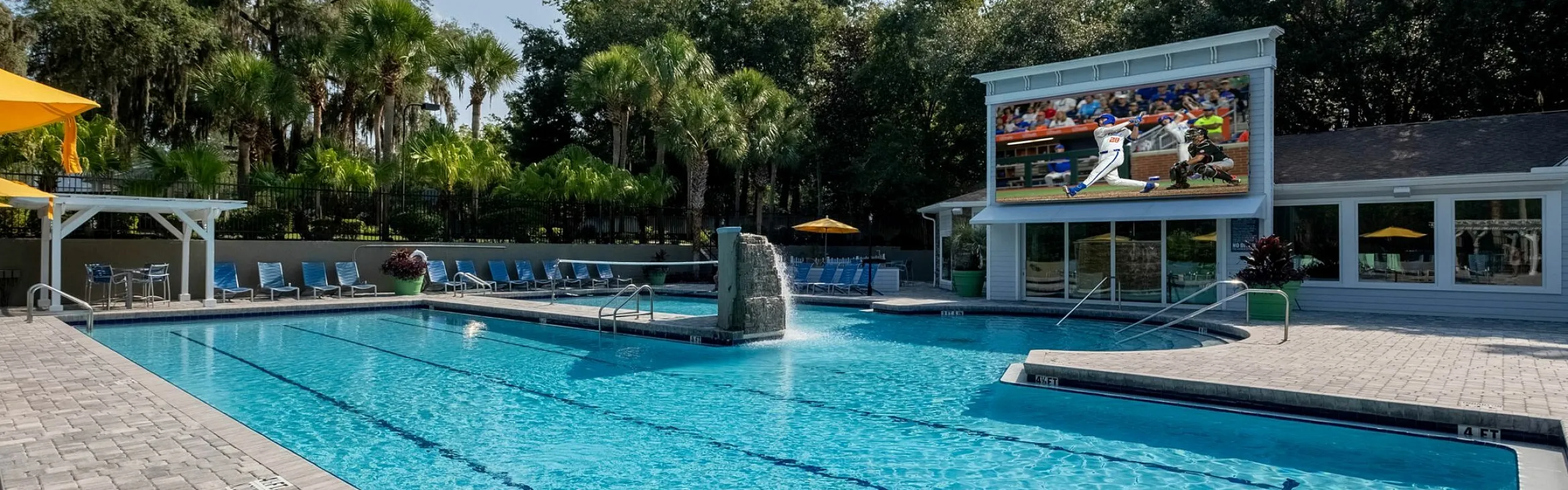 Luxurious outdoor swimming pool area with lounge chairs, surrounded by lush greenery, featuring a large poolside screen for entertainment.