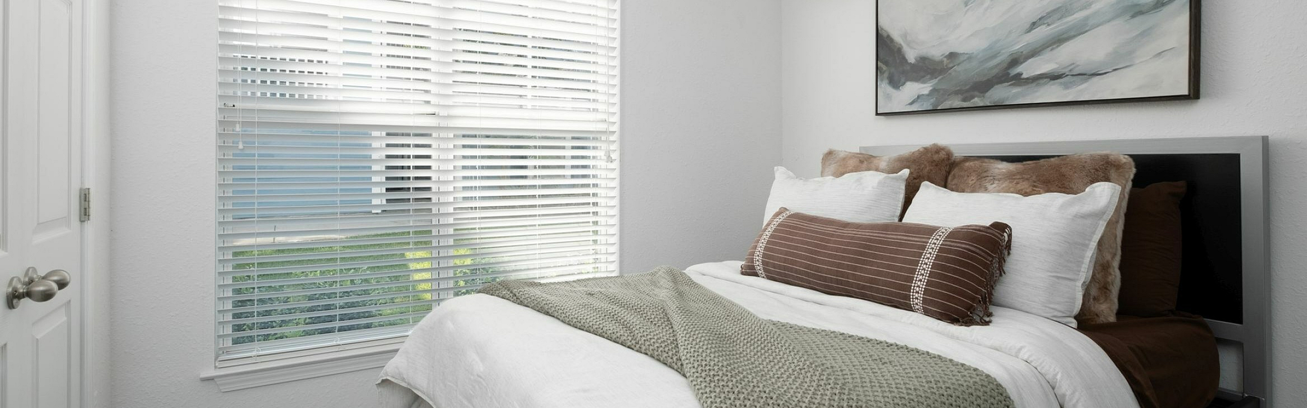 Bright and cozy bedroom featuring a plush bed with green and brown accents, a modern ceiling fan, and ample natural light through large windows.