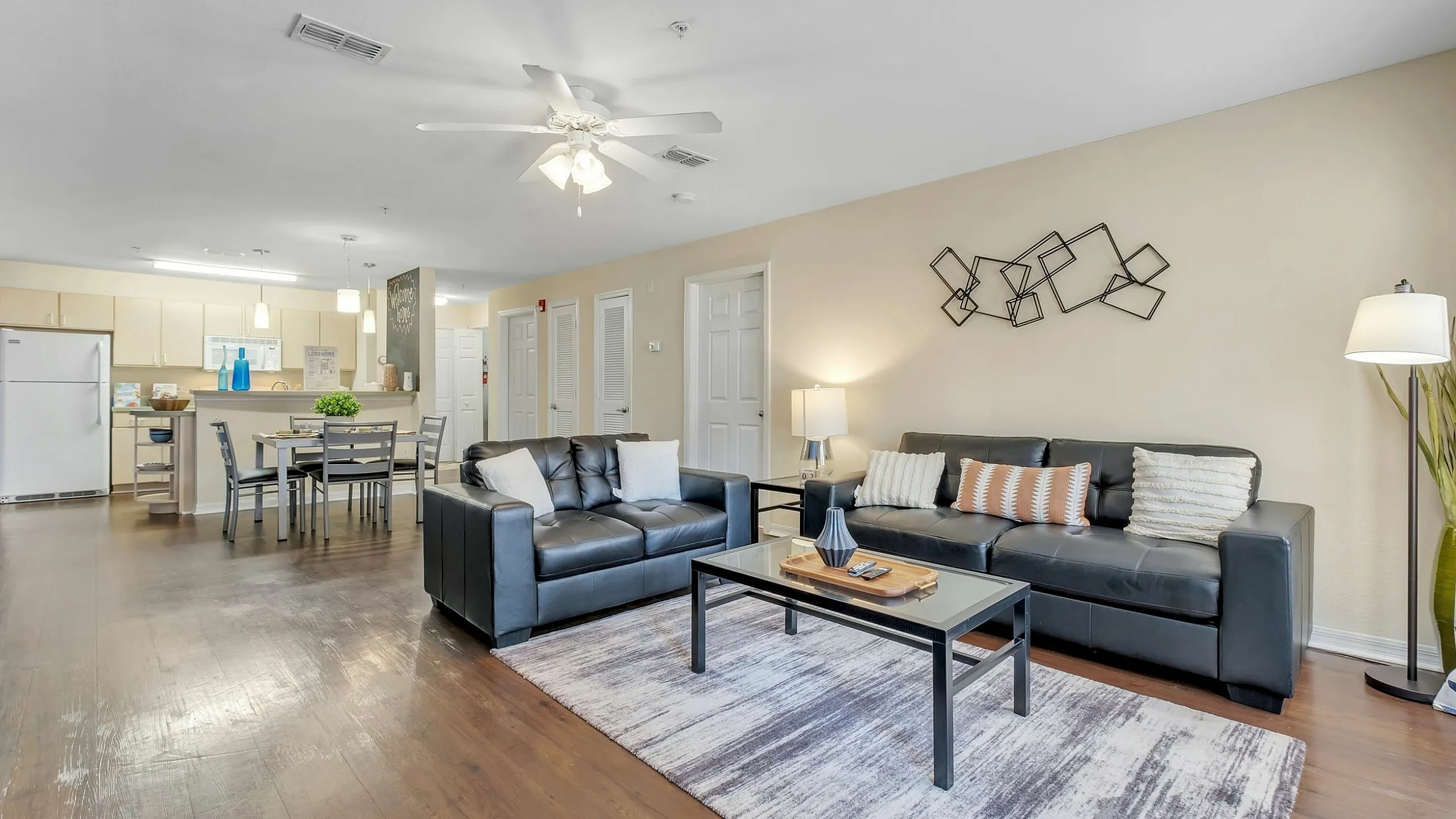 Modern open-concept apartment living room with elegant leather sofas, chic decor, and a contemporary kitchen area in the background.