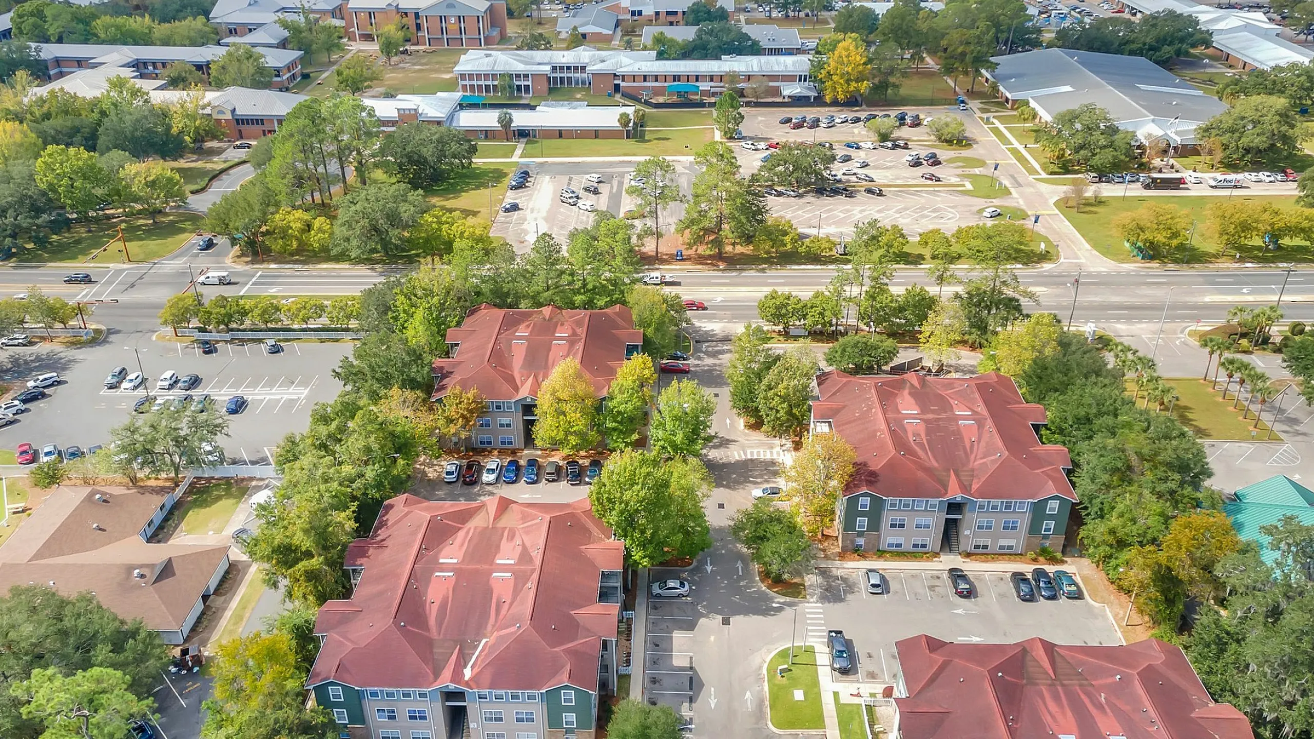 Breathtaking aerial view of a modern apartment complex with red rooftops surrounded by lush greenery, showcasing ample parking and a community pool.