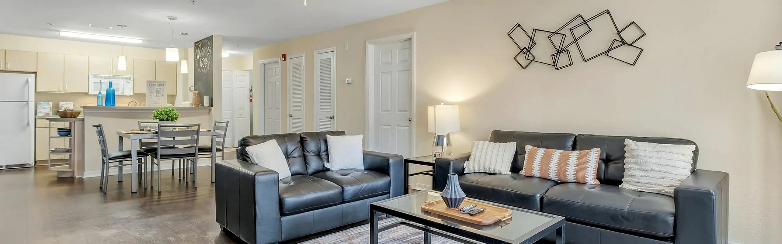 Chic open-concept living space featuring sleek black leather sofas, modern wall art, and a cozy dining area next to a stylish kitchen.