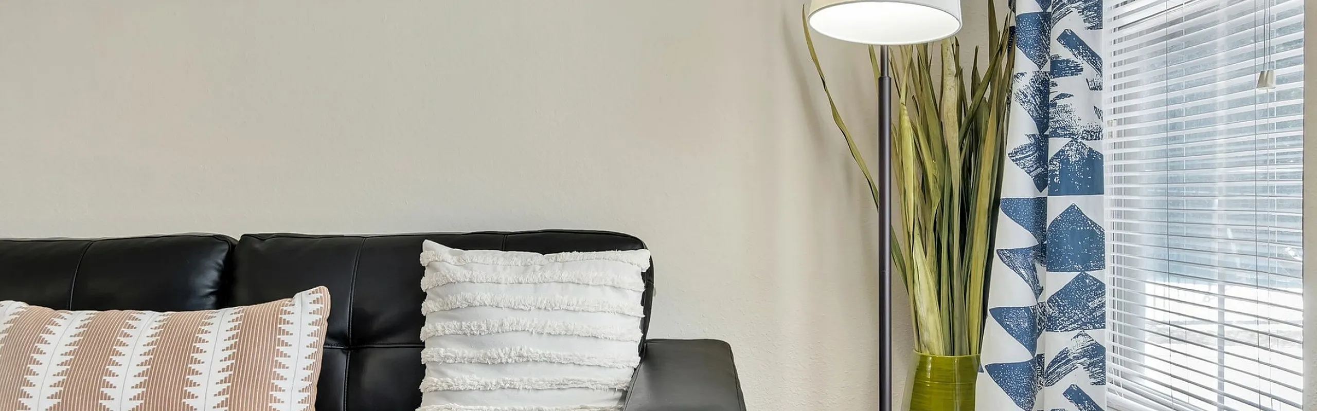 Chic modern living room featuring a black leather sofa with decorative cushions, elegant floor lamp, and stylish geometric wall art.