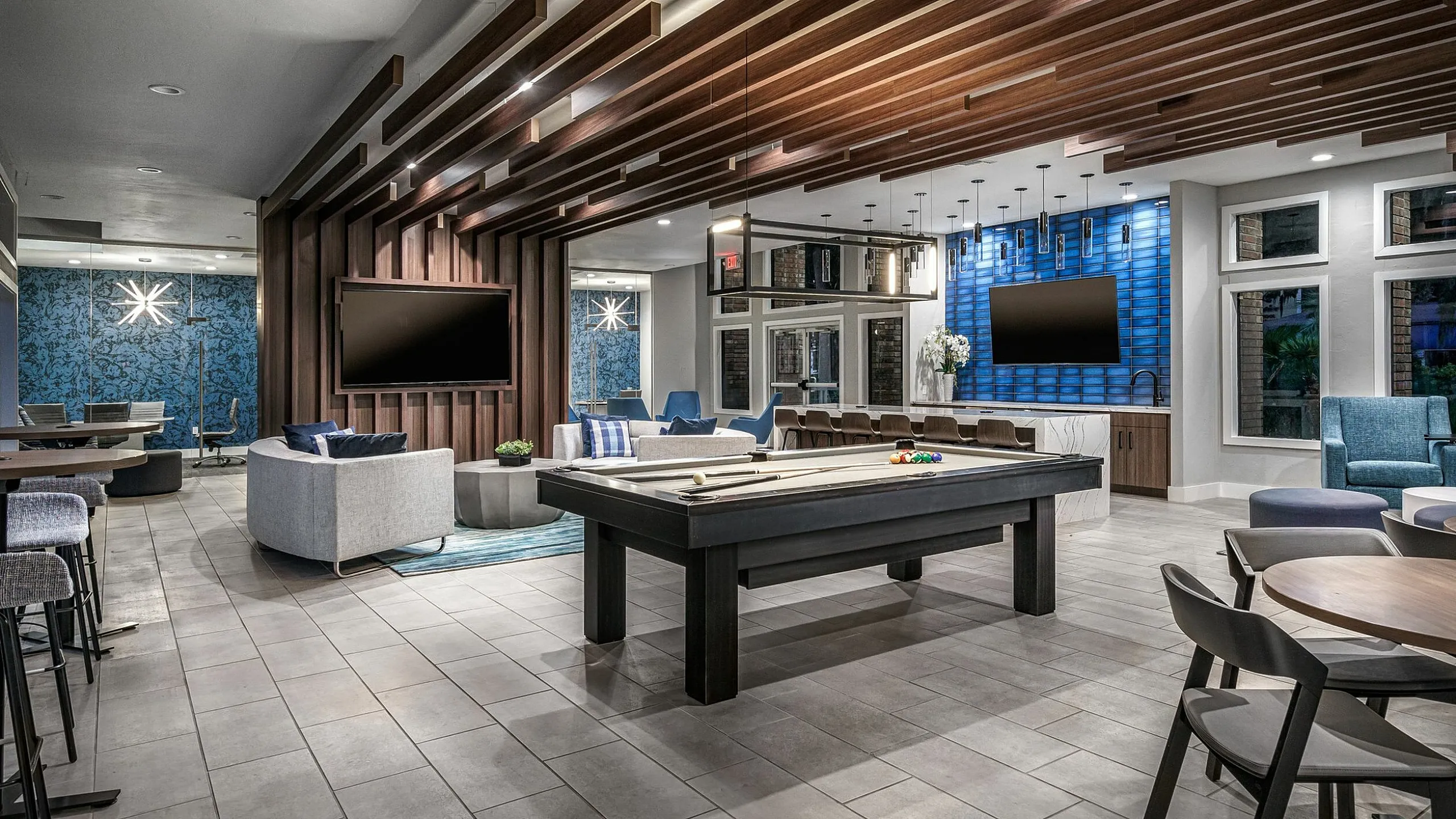 Luxurious modern lounge with stylish seating, pool table, and dual large-screen TVs, featuring elegant lighting and rich wood accents.