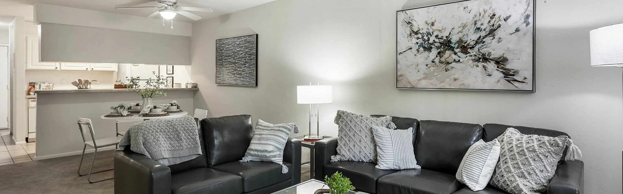 Modern living room with sleek black leather couches, contemporary artwork, and a stylish glass coffee table creating a cozy and inviting atmosphere.