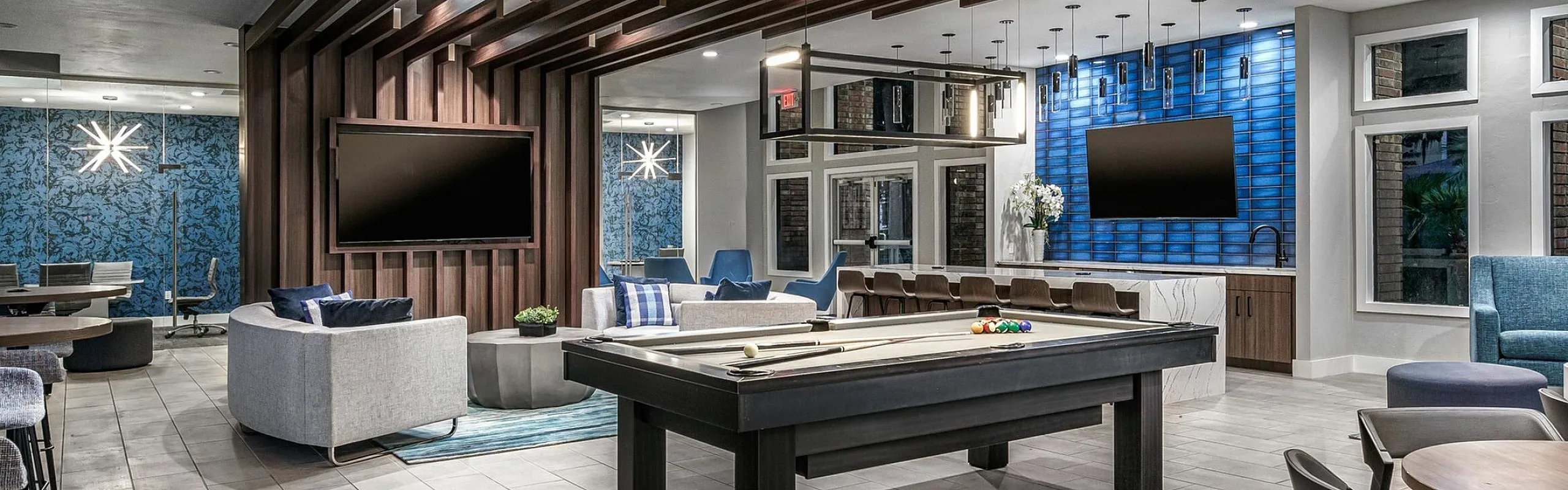Luxurious apartment recreation area with modern decor, featuring a stylish pool table, sleek seating arrangements, and dual large-screen TVs.