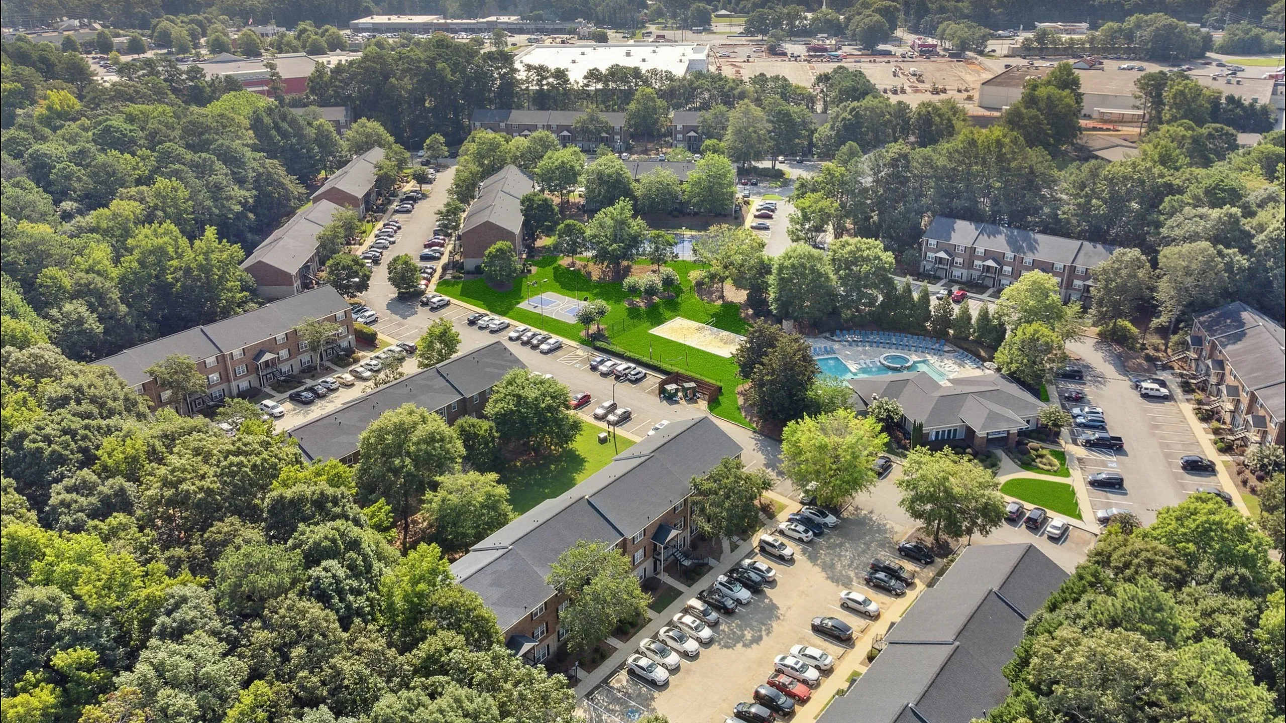 Inviting aerial view of a vibrant apartment community nestled in lush greenery with spacious parking, well-maintained pathways, and a sparkling swimming pool.
