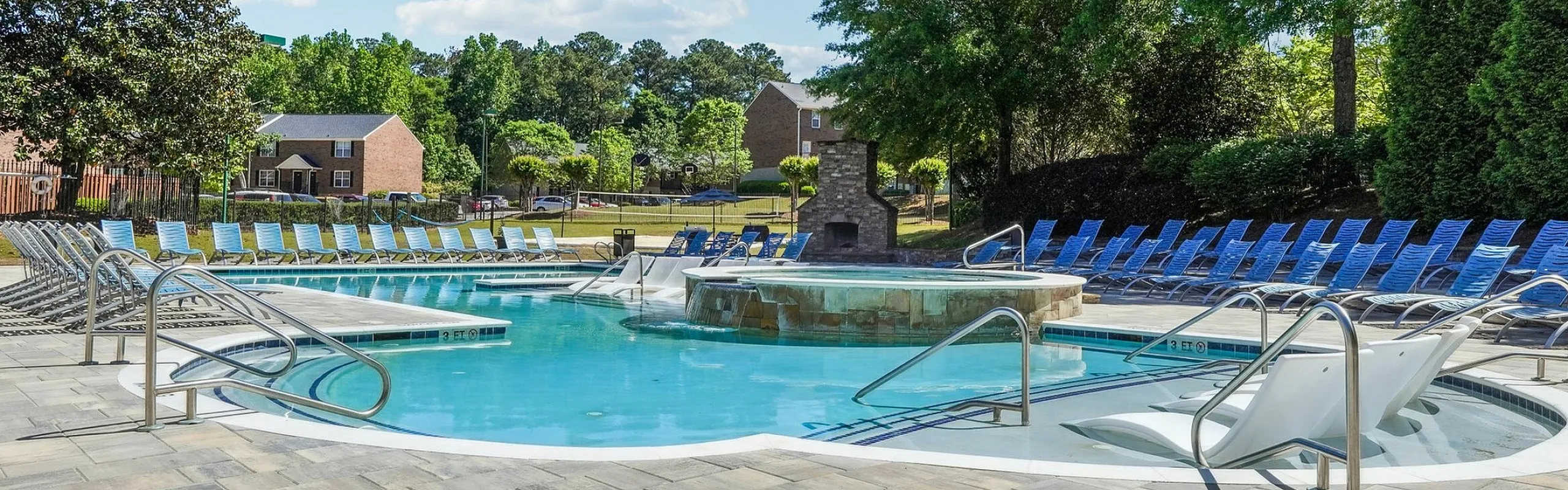 Inviting outdoor pool area featuring ample seating and lush greenery, ideal for relaxation and summer gatherings.