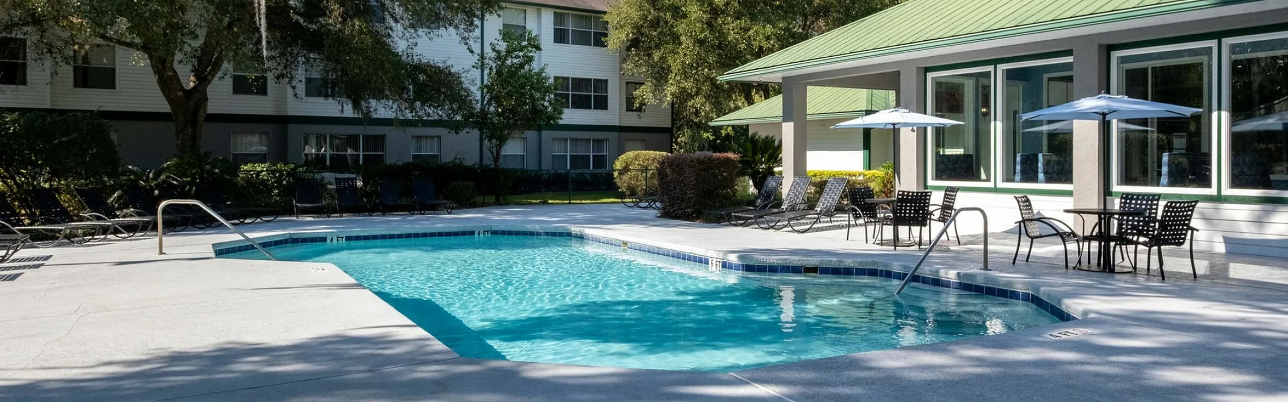 Inviting community pool area with modern loungers, shaded tables, and lush greenery.