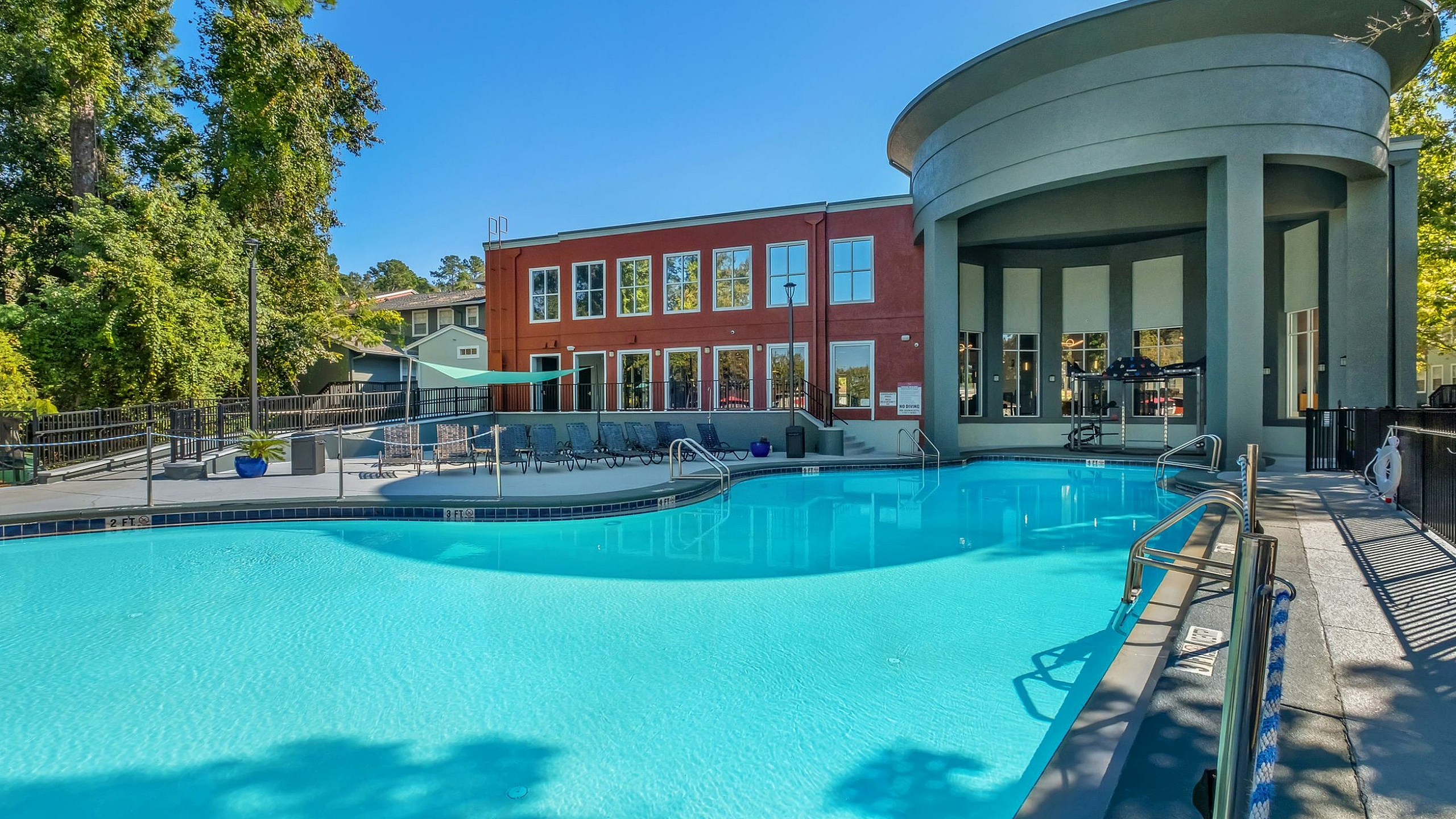 Luxurious apartment complex featuring a stunning outdoor pool with a modern clubhouse backdrop, surrounded by lush greenery and serene ambiance.
