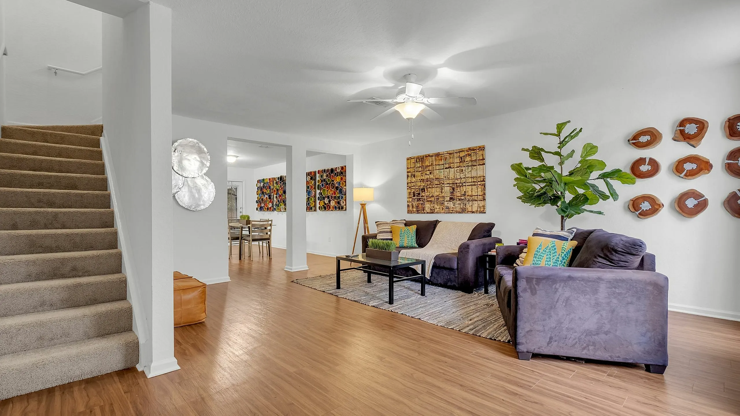 Inviting modern living room with plush seating, vibrant artwork, and an open layout leading to a stylish dining area. Elegant hardwood flooring and cozy neutral tones create a warm ambiance.