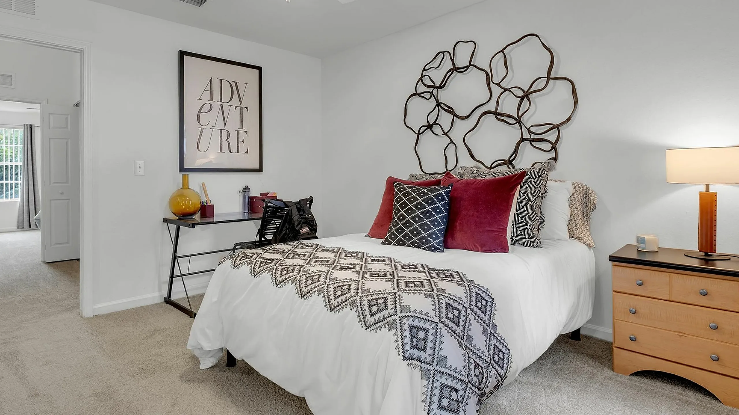 Chic bedroom with modern decor, featuring a cozy bed with patterned pillows, unique wall art, and a stylish nightstand lamp, inviting relaxation.