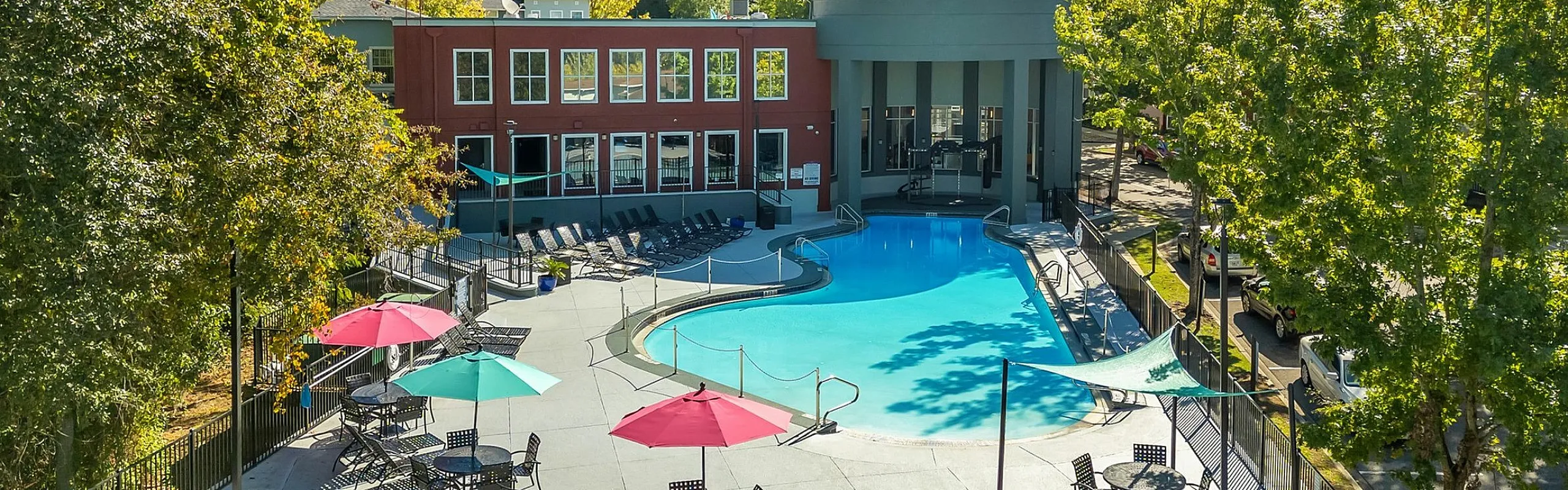 Luxurious apartment complex with a sparkling pool, vibrant umbrellas, and lush surroundings, perfect for relaxation and leisure.