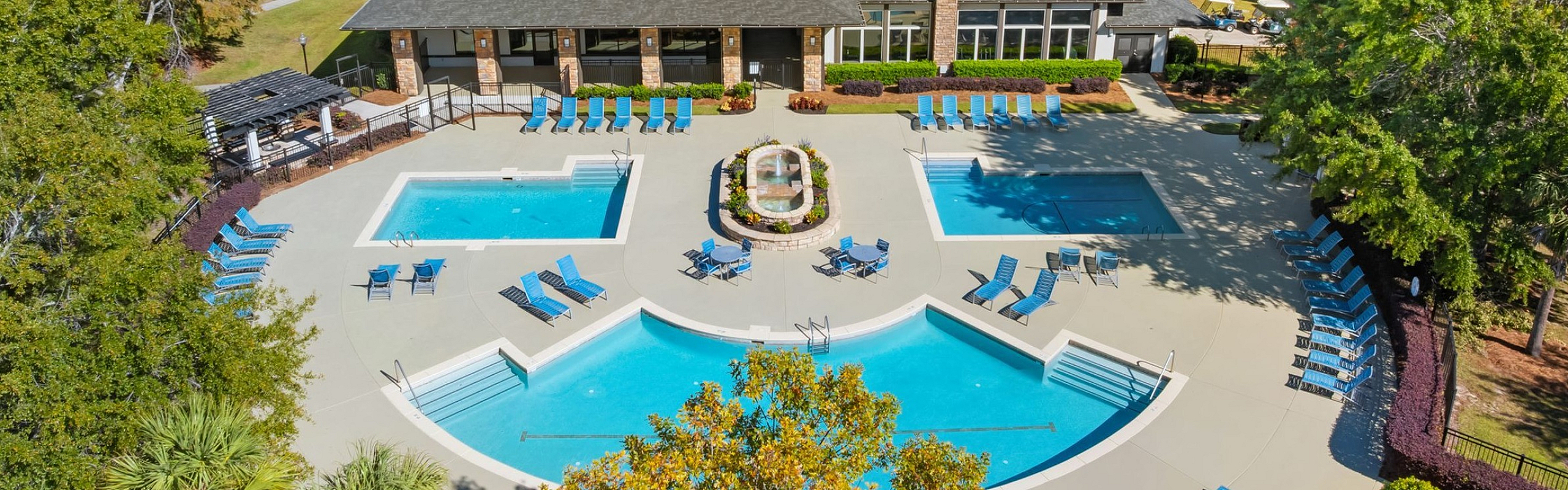 Aerial view of luxurious apartment complex with expansive pools, elegant lounge areas, and beautiful landscaping, perfect for relaxation and recreation.
