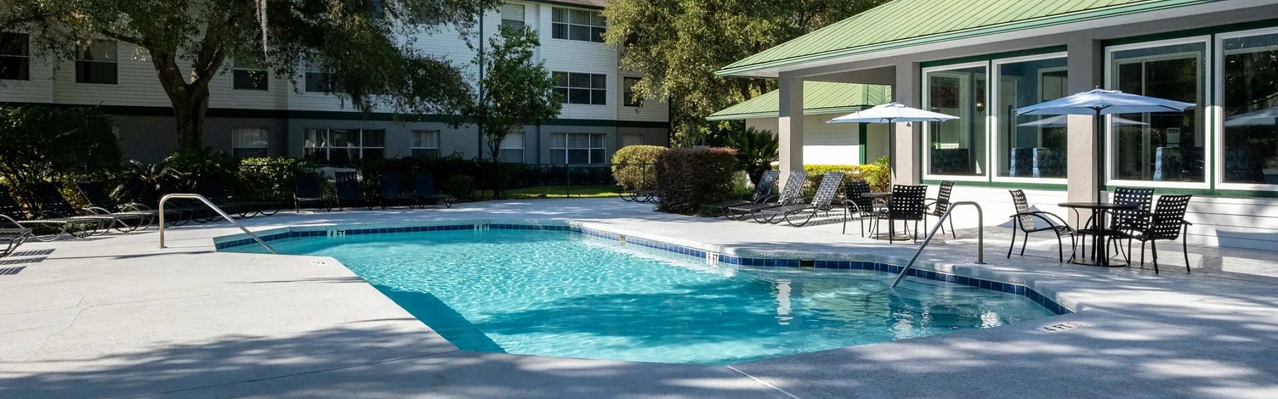 Elegant apartment complex with a sparkling outdoor pool, surrounded by lush greenery and stylish patio seating, perfect for relaxation and leisure.