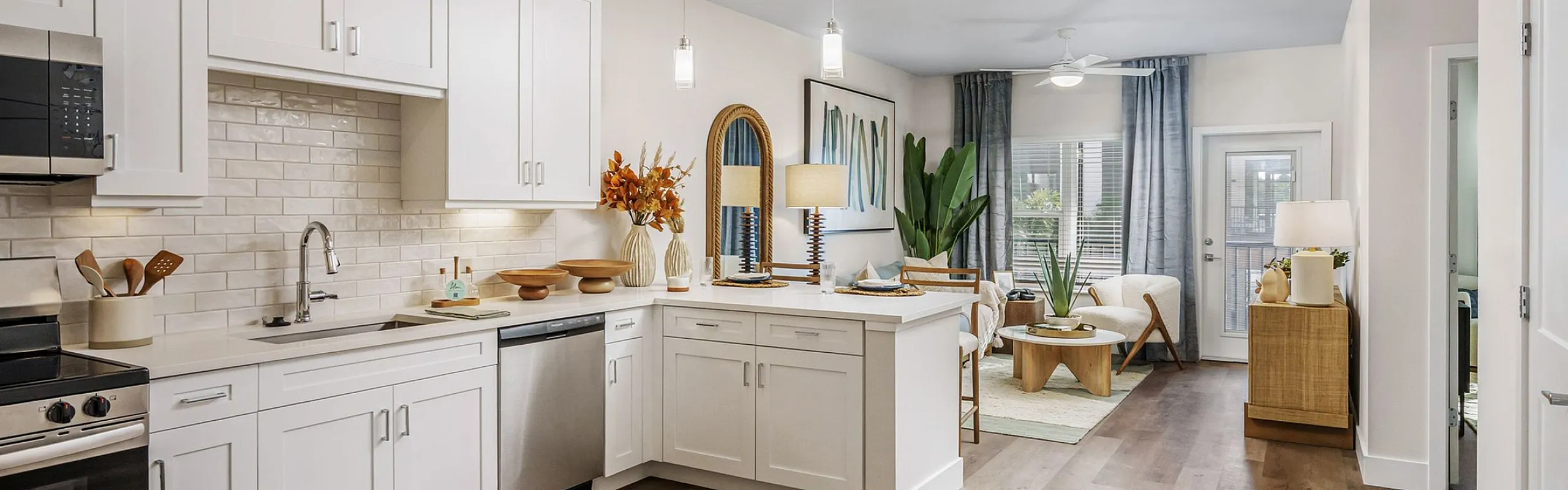Elegant open-concept living space with a modern kitchen featuring white cabinets, stainless steel appliances, and a cozy living area with warm wooden floors and stylish decor.