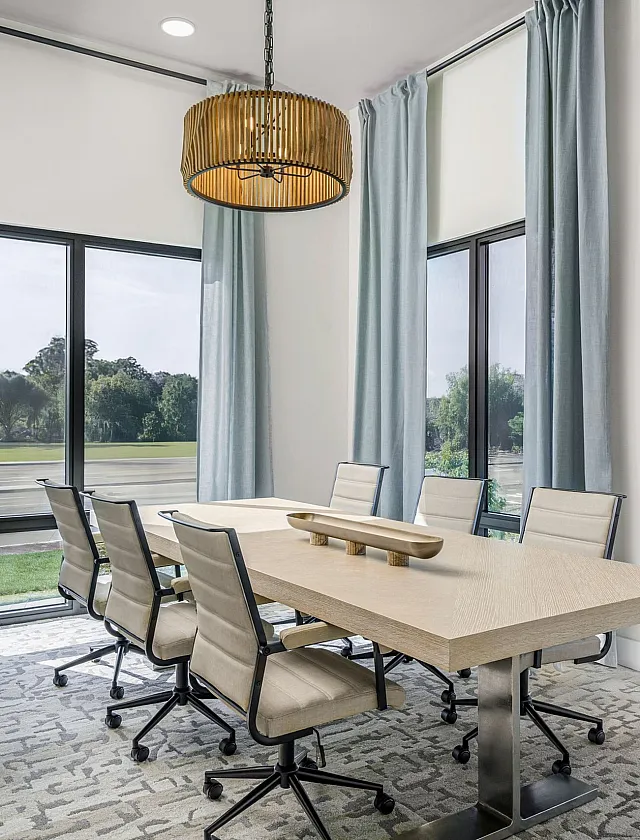 Elegant conference room with a large wooden table, sleek chairs, and floor-to-ceiling windows offering a beautiful view of lush greenery.