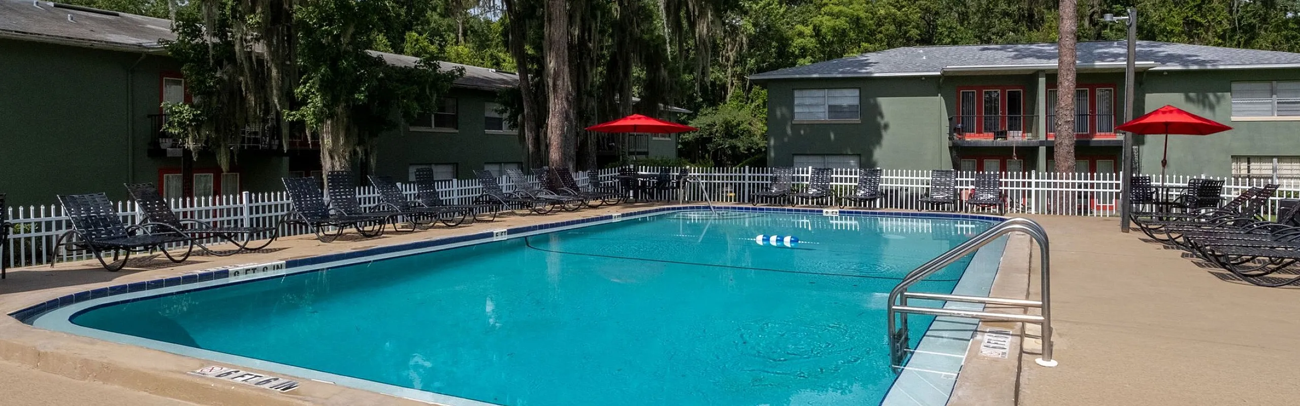 Inviting apartment complex with a pristine swimming pool, surrounded by lush trees and comfortable lounge chairs.