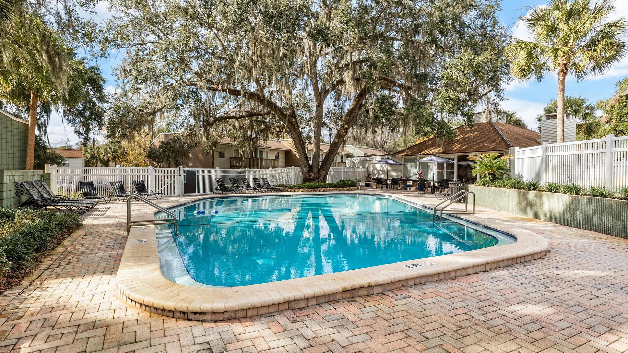 Inviting outdoor pool area surrounded by lush greenery, featuring sun loungers and a cozy clubhouse perfect for relaxation.