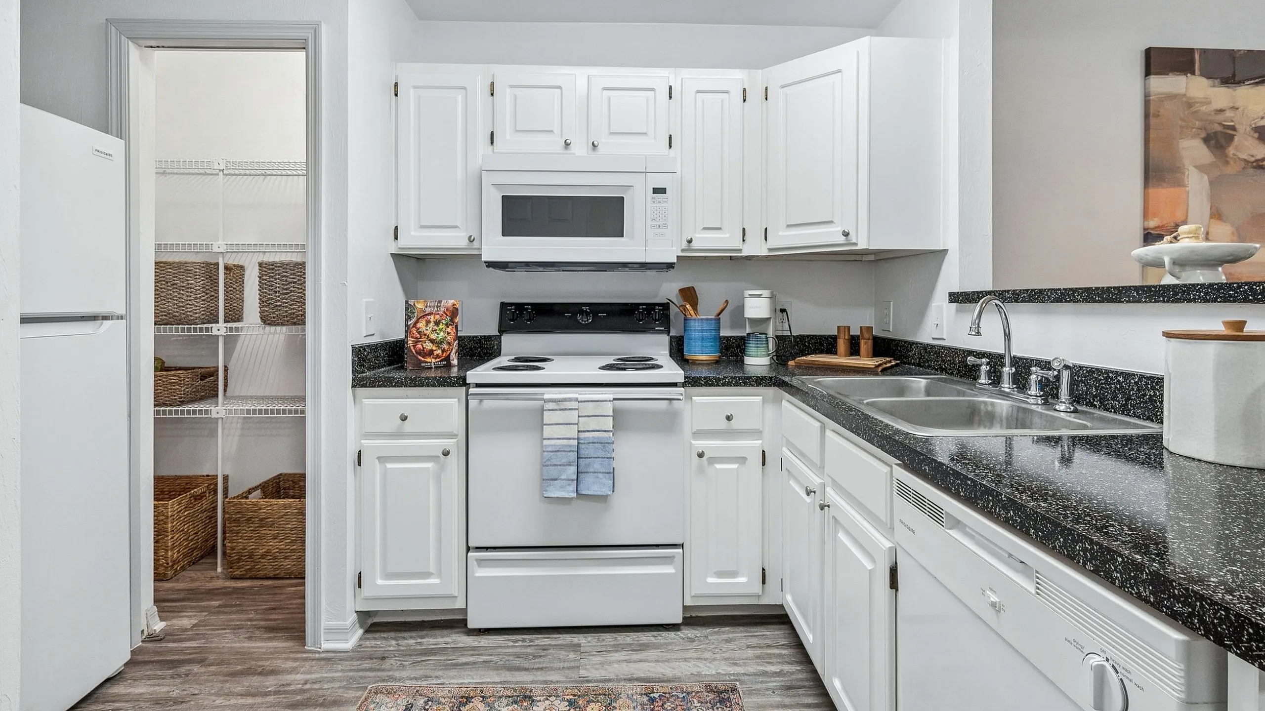 Charming kitchen with white cabinetry, modern appliances, and a cozy pantry, enhanced by a stylish rug and black granite countertops.
