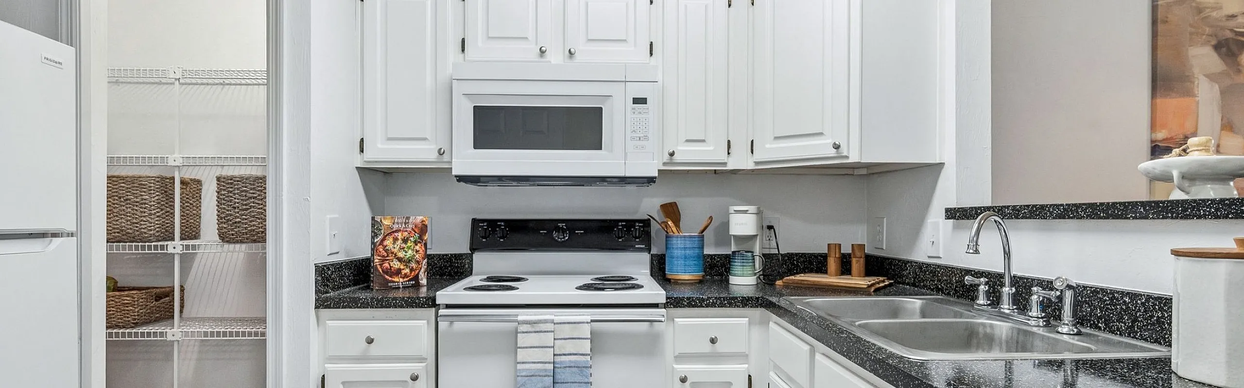 Elegant kitchen with white cabinetry, modern appliances, and a spacious layout featuring a pantry. The room is complemented by sleek black countertops and a stylish vintage rug.