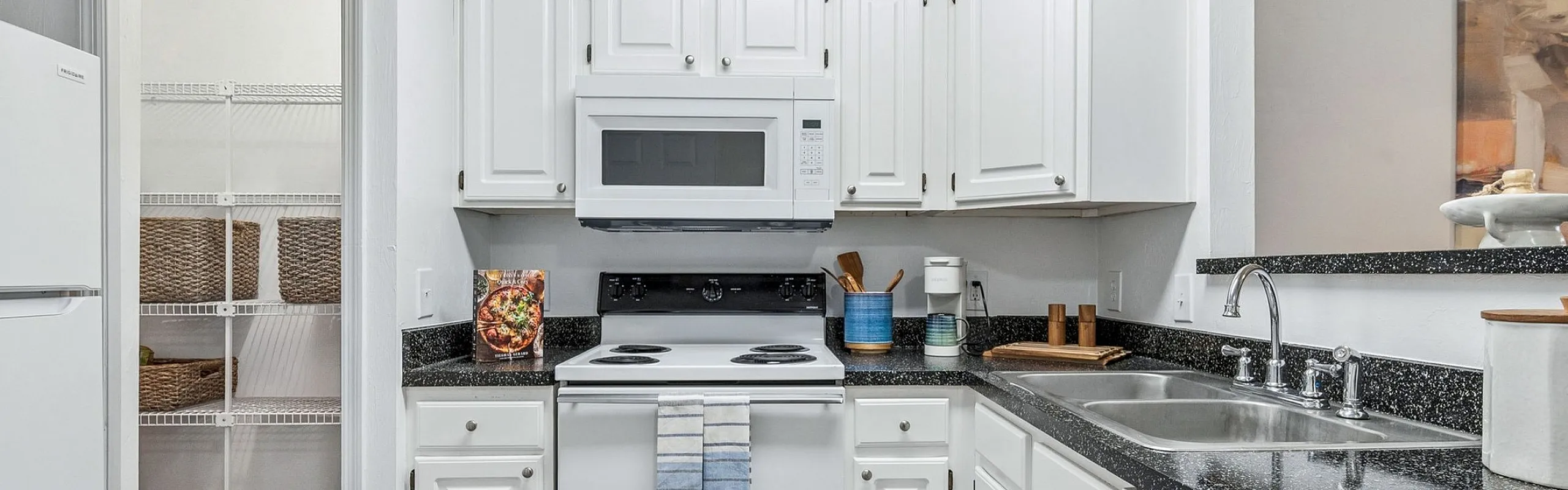 Charming kitchen with sleek black countertops, white cabinetry, and modern appliances, featuring a cozy pantry and stylish rug.