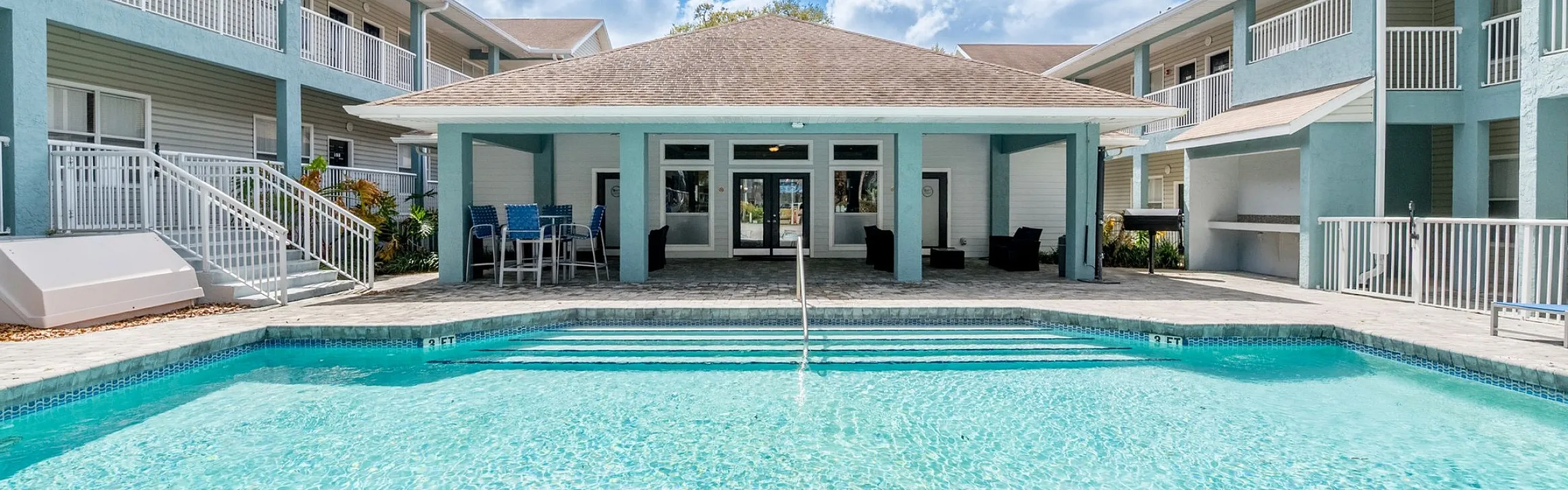 Inviting apartment complex featuring a sparkling pool and spacious sun deck, perfect for relaxation under the bright blue sky.