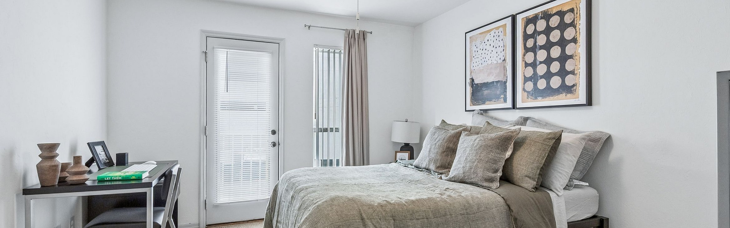 Chic bedroom featuring a cozy bed with stylish linens, modern art, and natural light from the glass door, creating an inviting and restful atmosphere.