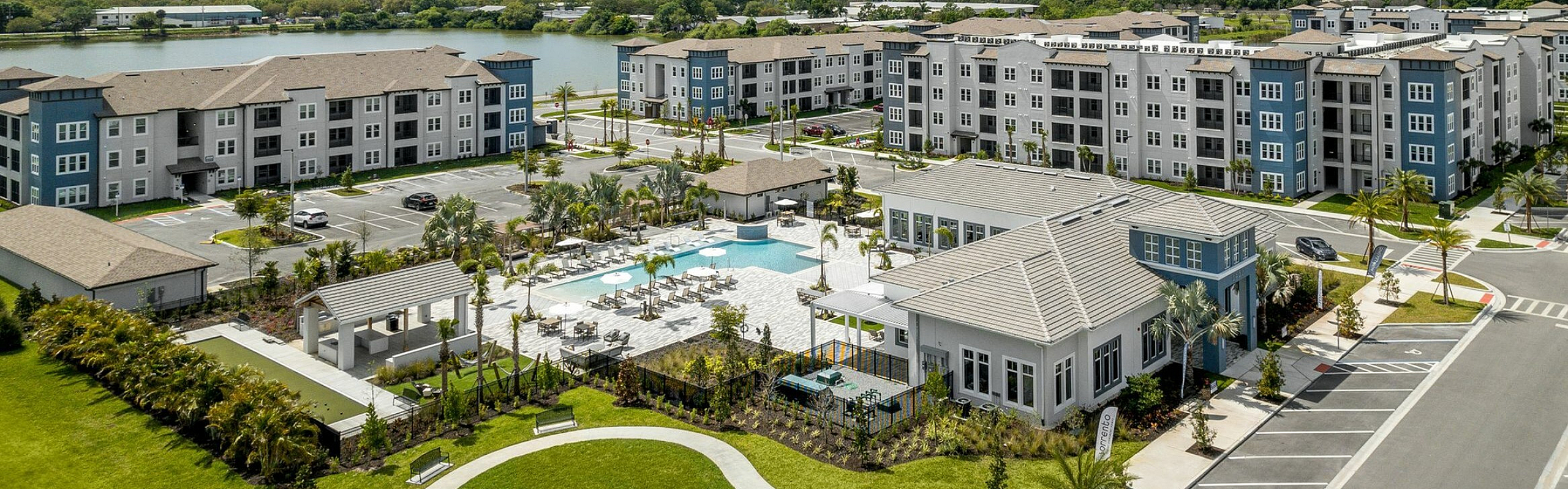 Vibrant apartment complex with modern architecture, lush landscaping, and a refreshing swimming pool under a bright blue sky.